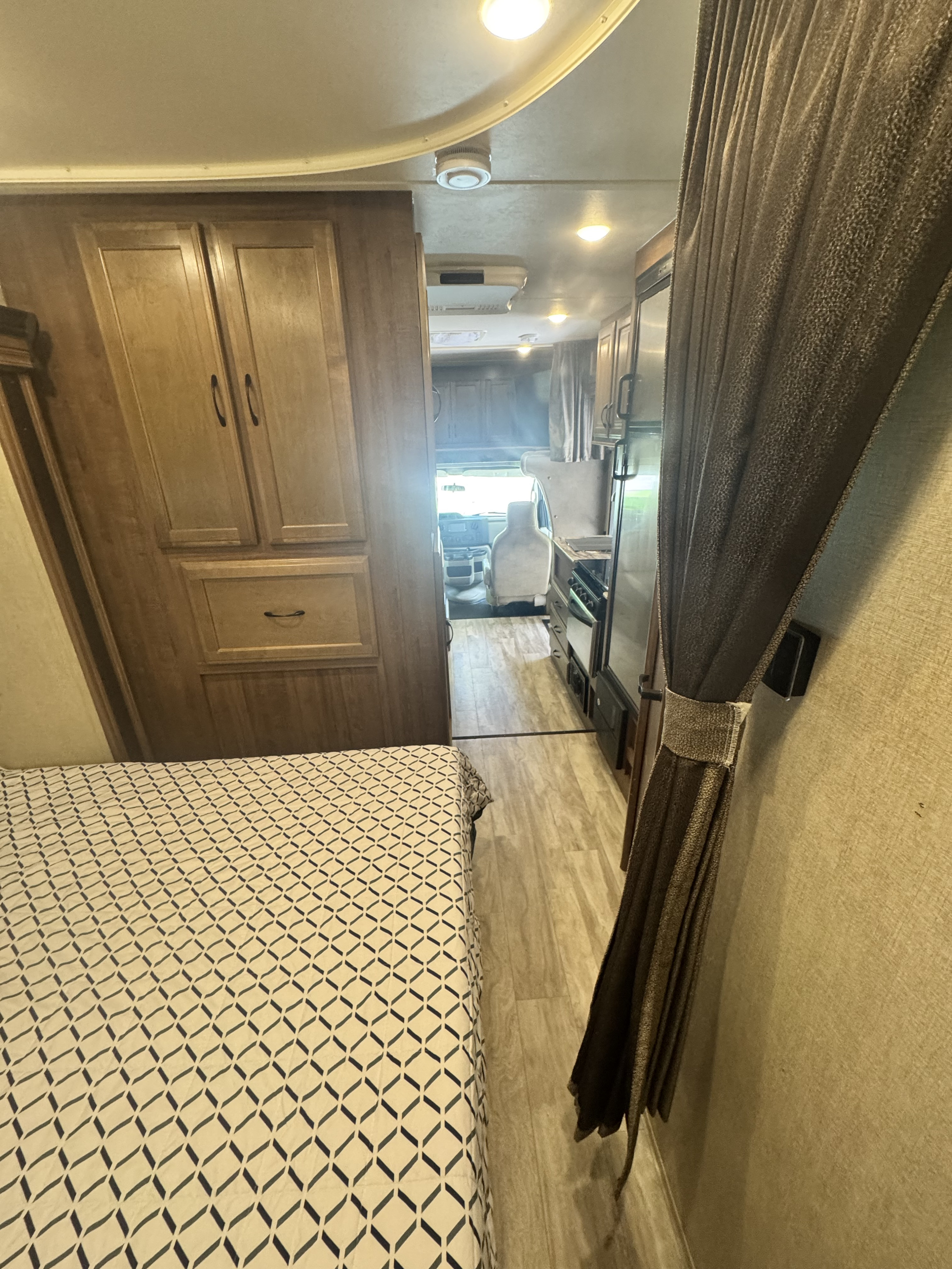 Spacious RV rental interior featuring a bedroom with patterned bedding, wood cabinets, a galley kitchen, and a view of the front cabin.. Gulf Stream Conquest 2019