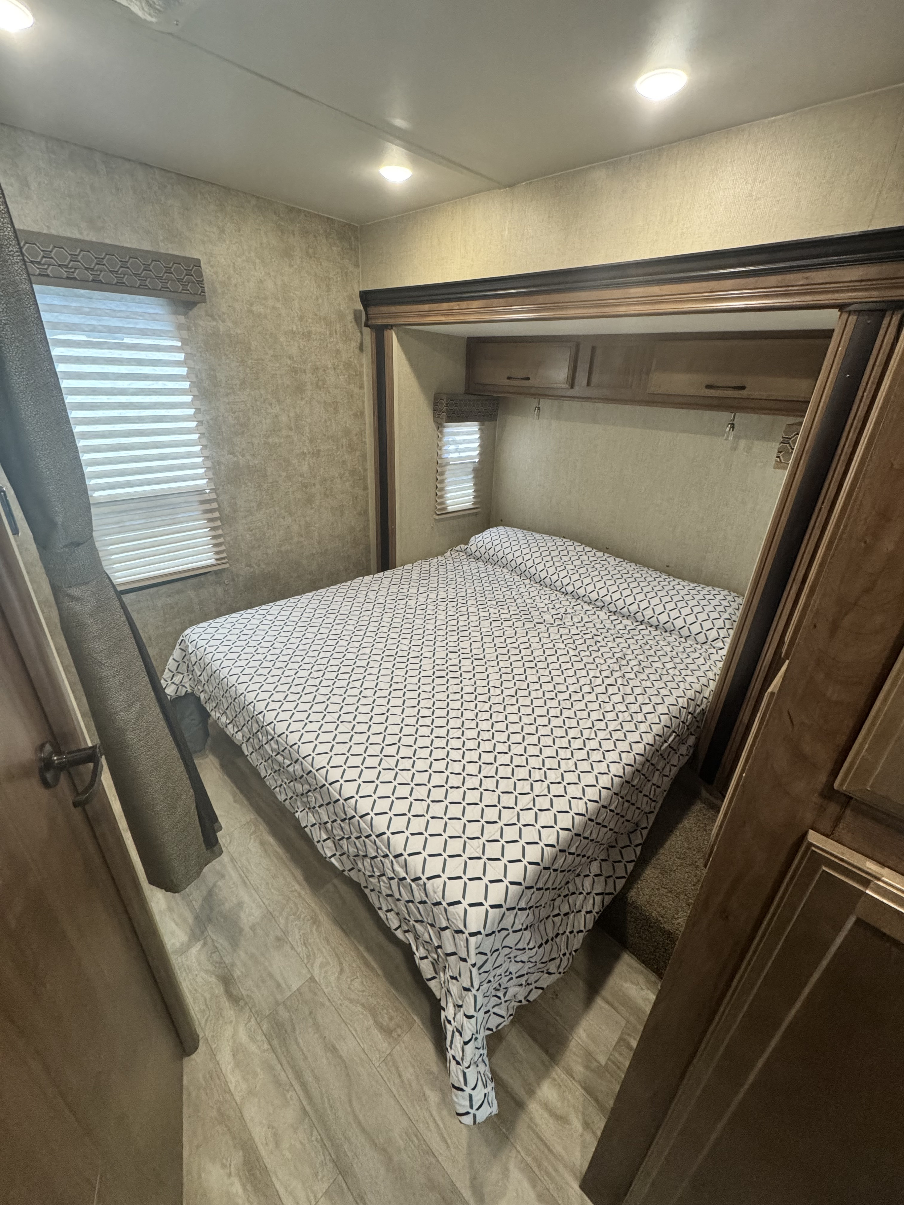 Comfortable RV rental bedroom showcasing a patterned bed, wood trim, blinds, and overhead cabinets.. Gulf Stream Conquest 2019