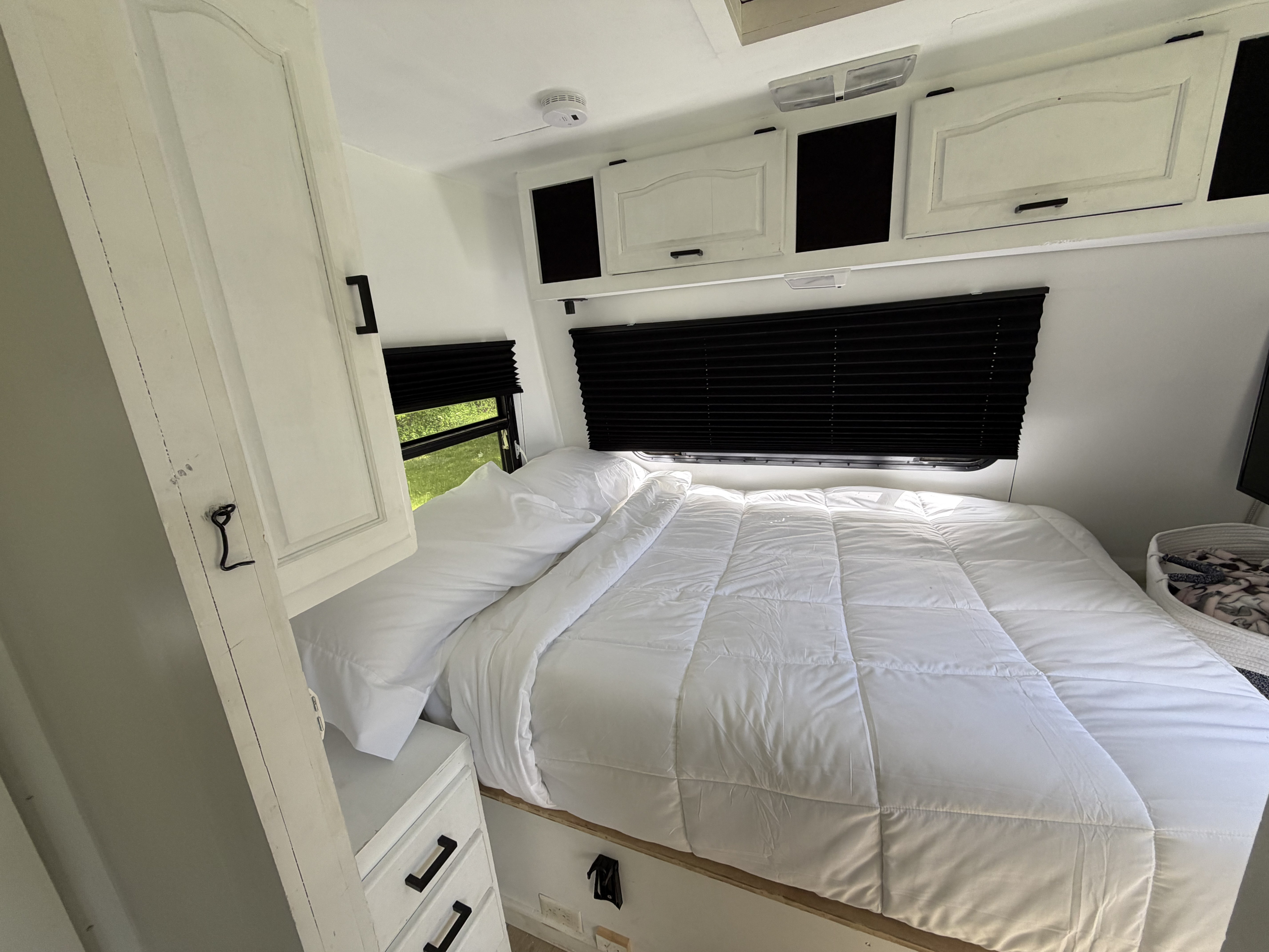 Bright and modern RV rental bedroom featuring white bedding, black privacy blinds, and convenient overhead storage cabinets.. Thor Motor Coach Citation 1999