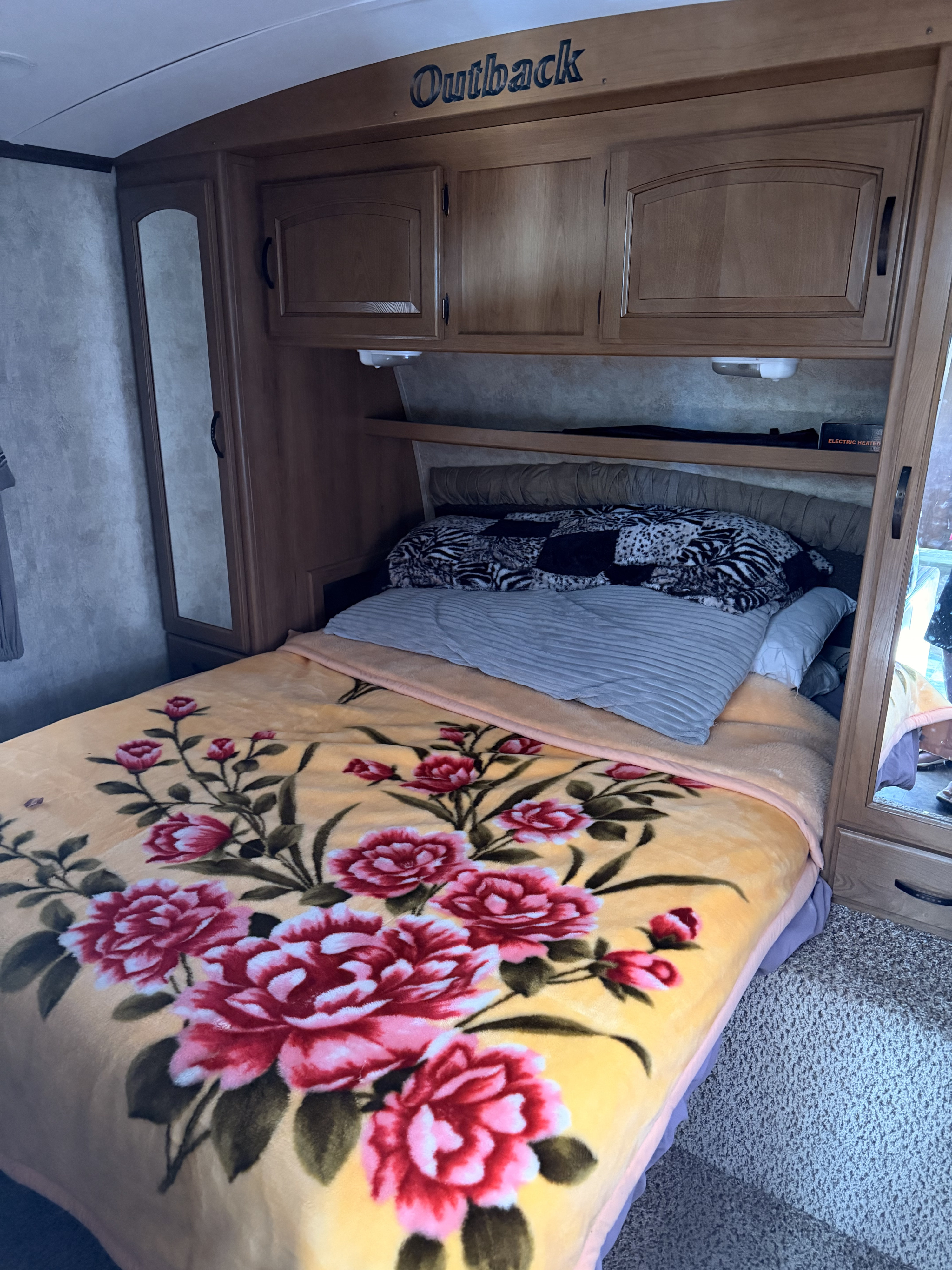 Cozy rv rental bedroom featuring a bed with a vibrant yellow floral blanket, wooden Outback cabinets, and mirrored closet doors.. Keystone RV Outback 2011