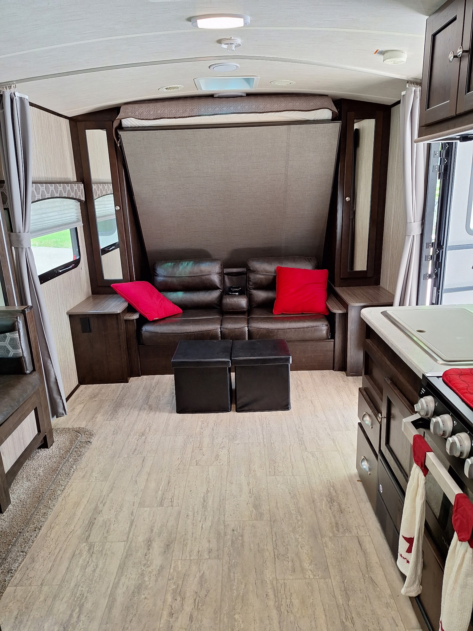 RV rental interior with a clever fold-down bed, dark leather seating, and a partial view of the kitchen counter and stove.. Cruiser RV Shadow Cruiser 2018