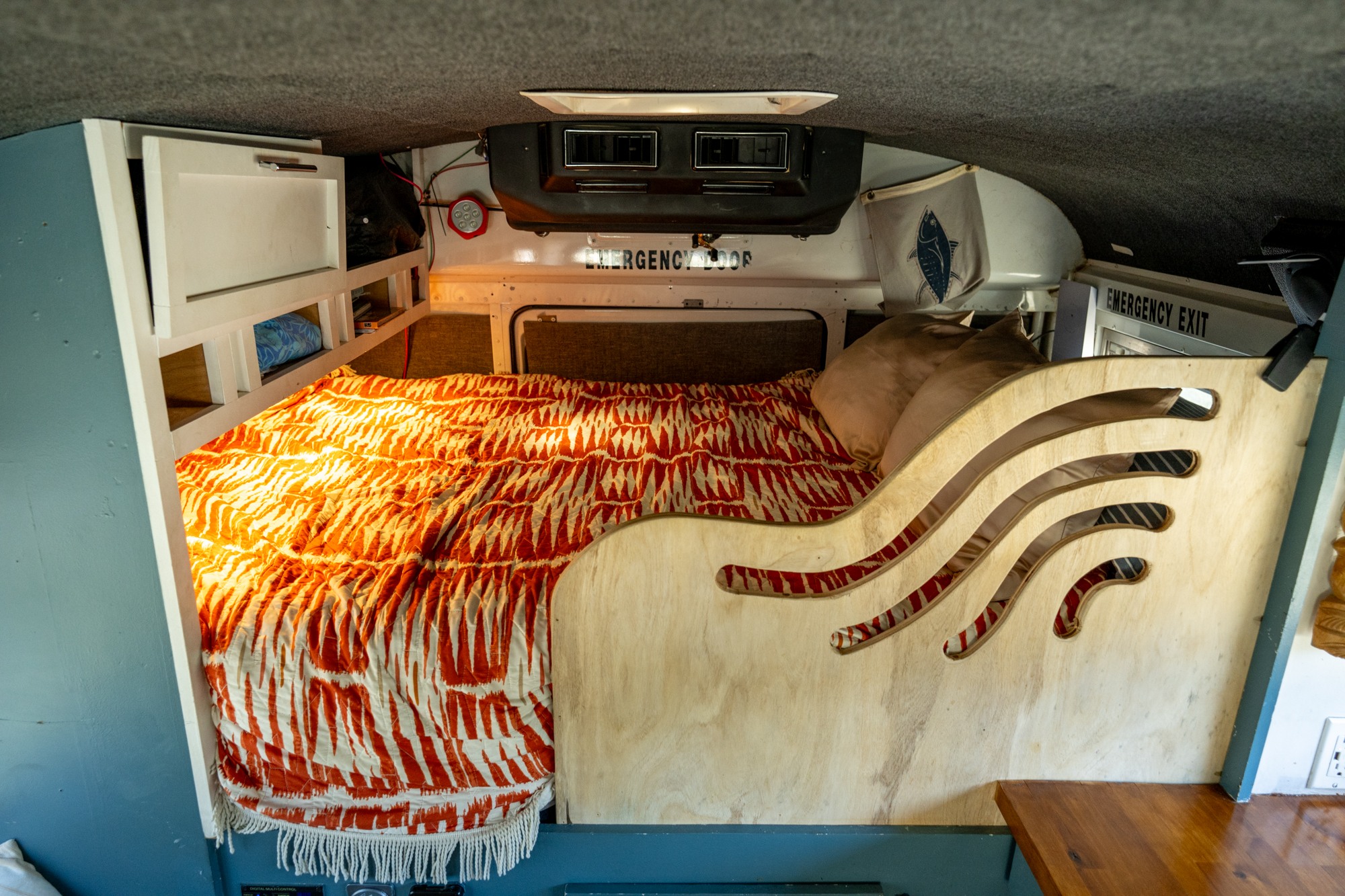 Cozy RV rental sleeping area with warm bedding, storage, and unique wave-cut wood paneling. Perfect for road trips!. Chevrolet Express s3500 2003