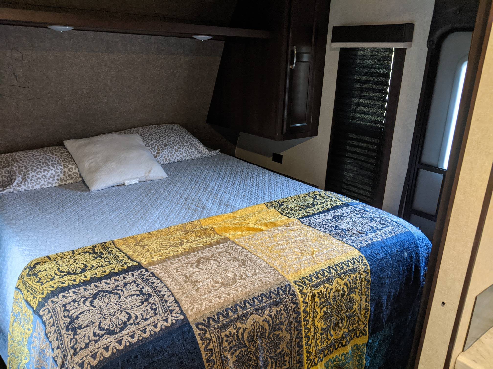 Cozy RV rental bedroom featuring a bed with a patterned throw, overhead storage, and a window for comfortable travel accommodation.. Jayco Jay Flight 2020