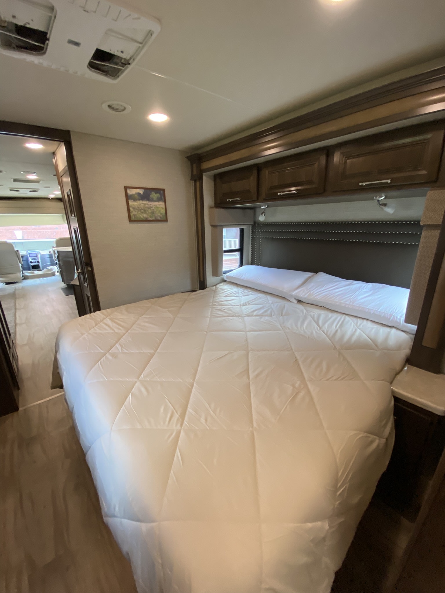 Spacious rv rental bedroom featuring a comfy bed, upholstered headboard, and storage cabinets. View into the motorhome's front.. Entegra Coach Emblem 2018