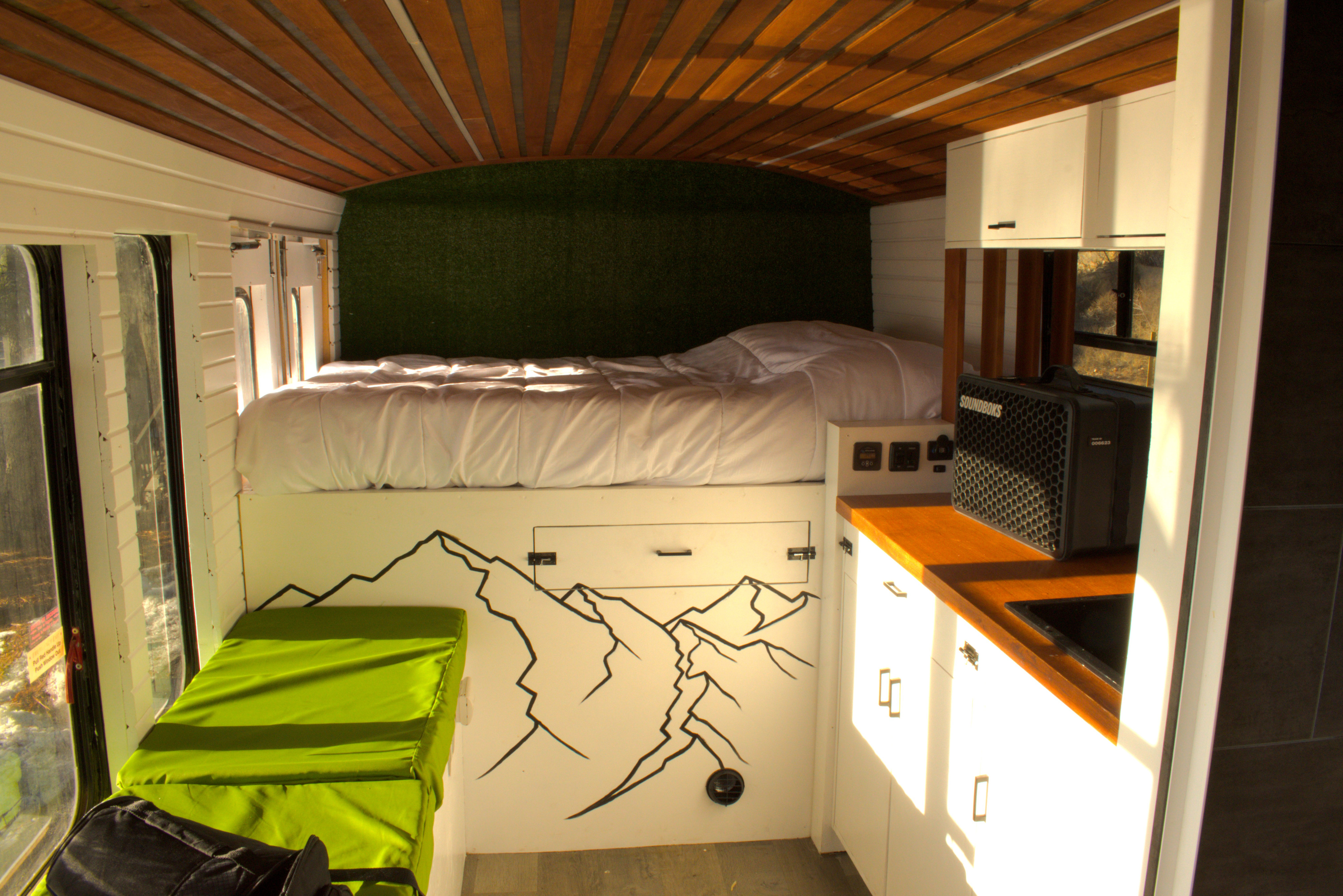 RV rental van interior: bed against a green wall, wood ceiling, kitchenette, & mountain art.. Ford Ford E350 2001