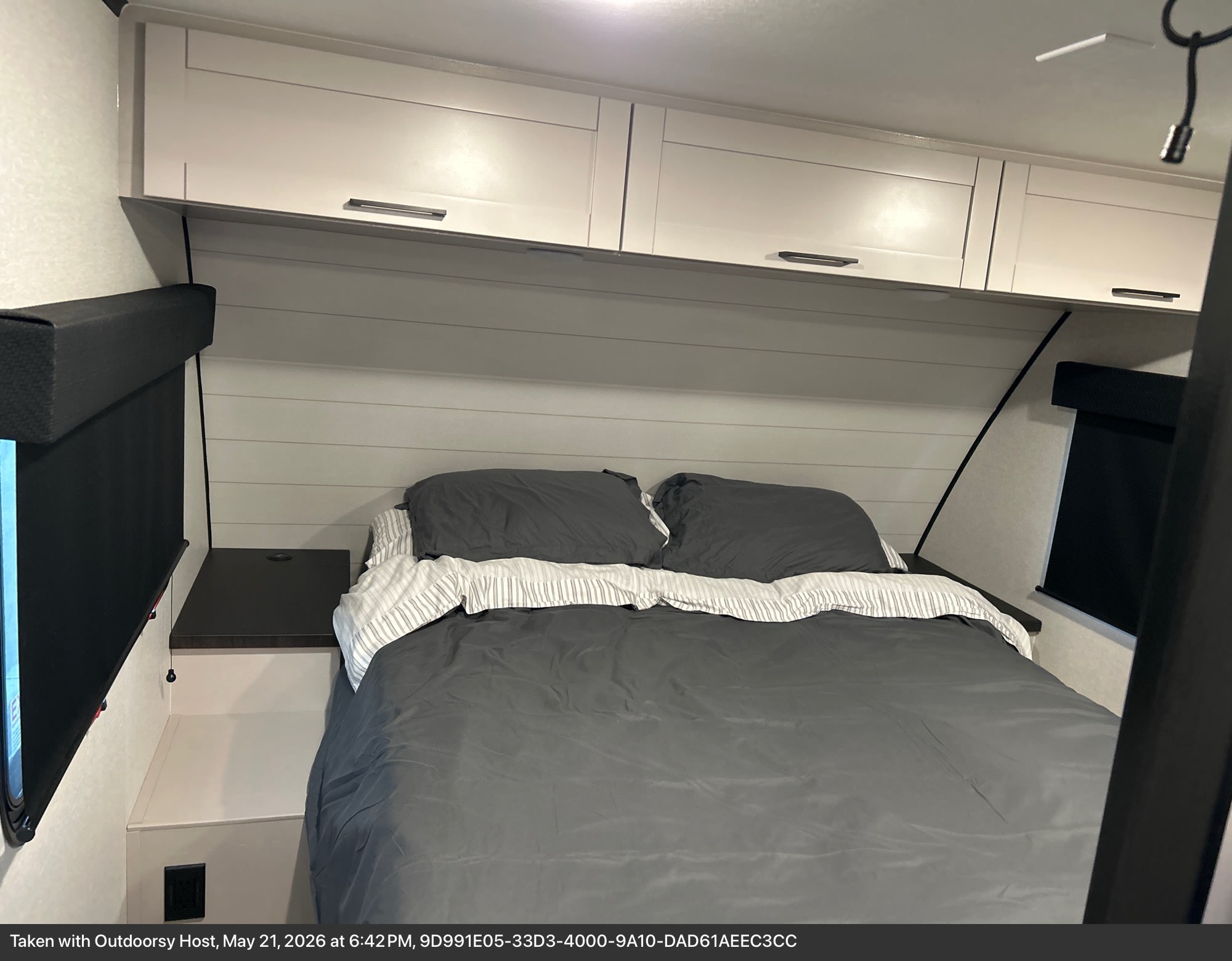 Comfortable RV rental bedroom featuring a bed with gray bedding, overhead cabinets, and roll-down window shades.. Jayco 29BHB 2026