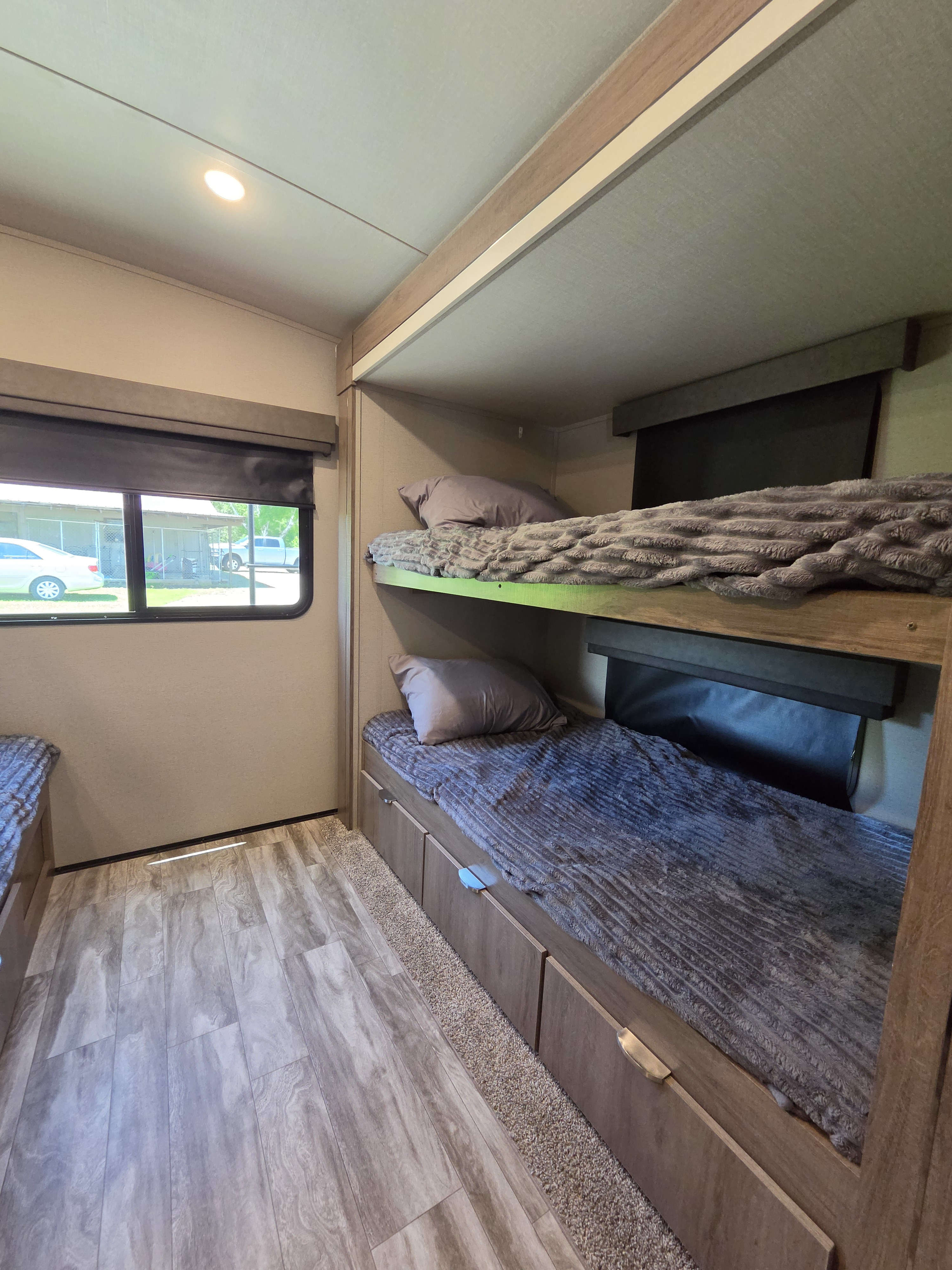 Inside this RV rental: two cozy bunk beds with pillows, blankets, and integrated storage drawers. A window offers an outdoor view.. Grand Design Imagine 2021