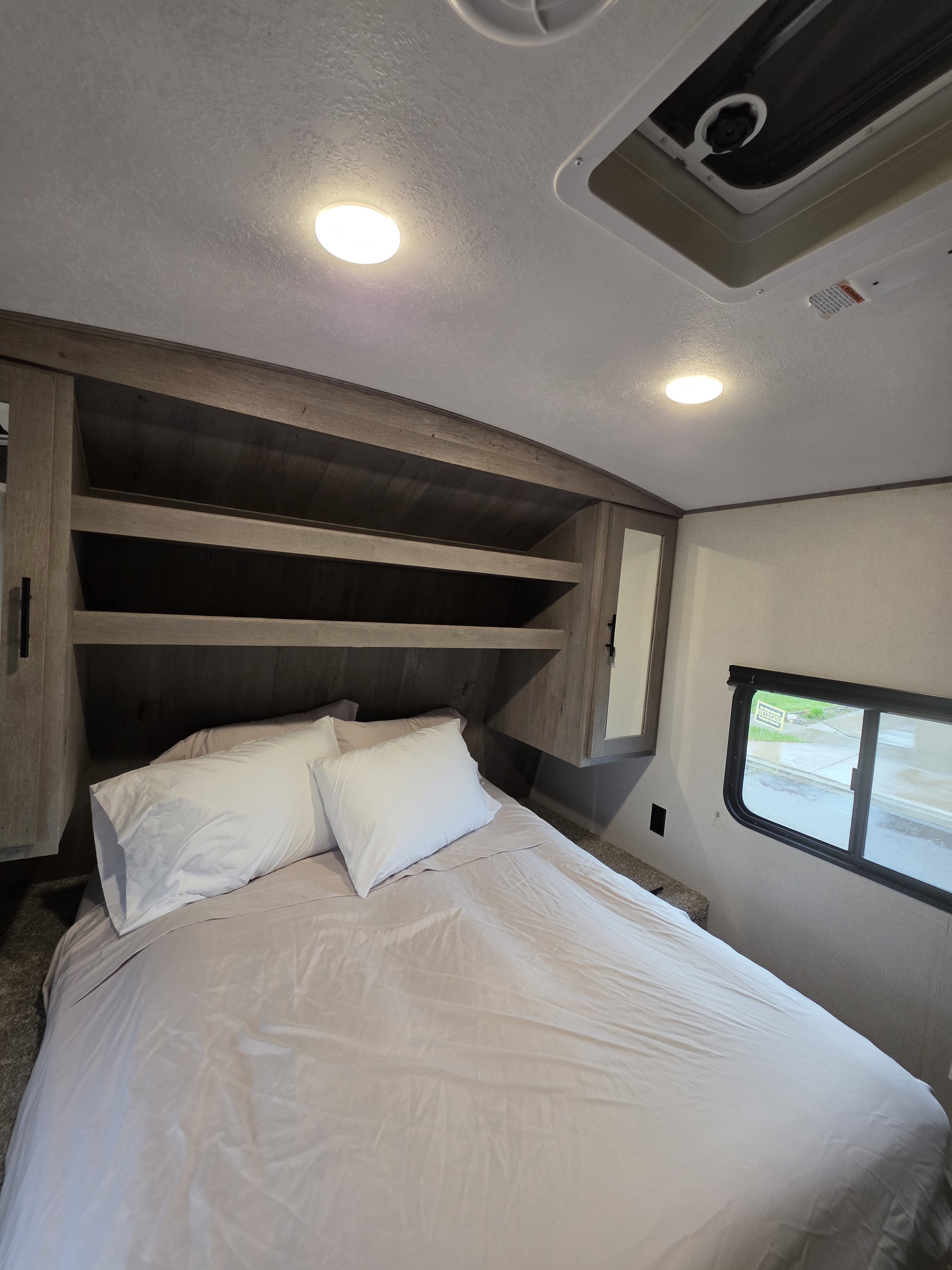 Modern RV rental bedroom featuring a cozy bed, ample overhead storage, a mirrored cabinet, and a window.. Keystone RV Springdale 2021