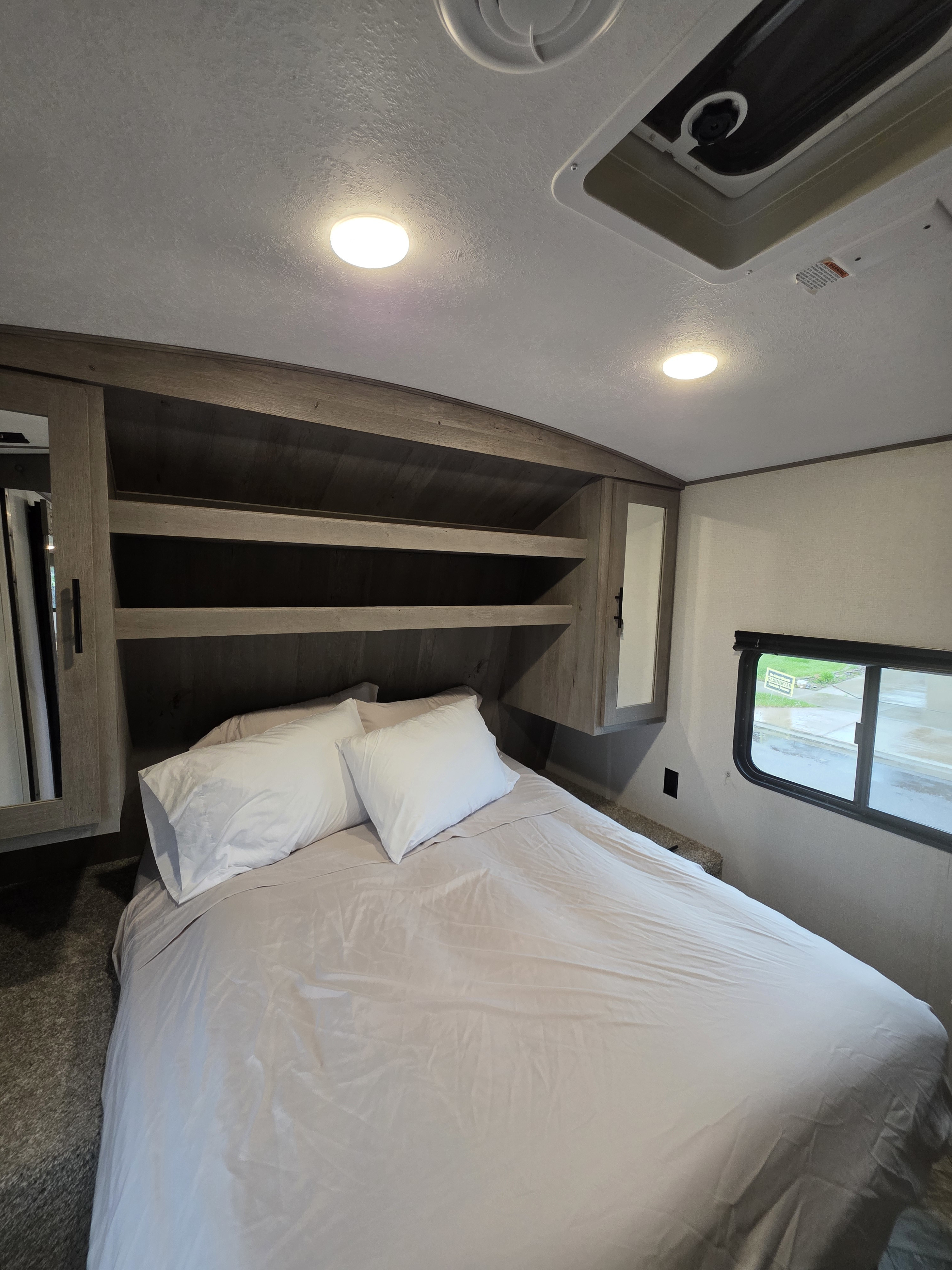 This inviting RV rental bedroom features a comfy bed, ample overhead storage, and a window view for relaxing travels.. Keystone RV Springdale 2021