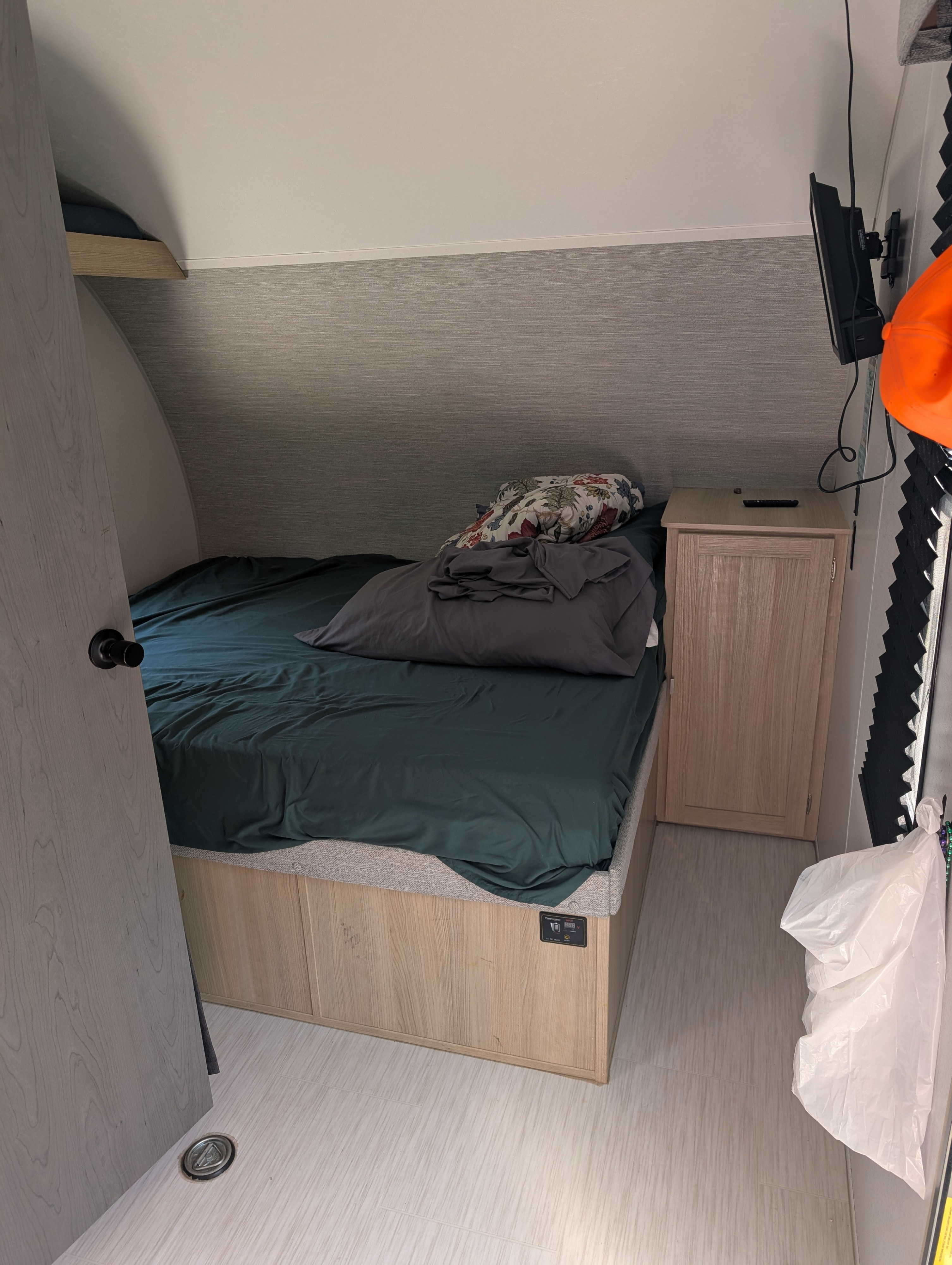Inside an RV rental bedroom: a bed with dark green sheets, wooden nightstand, and wall-mounted TV are visible.. Forest River Wildwood FSX Platinum Toy Hauler 2023