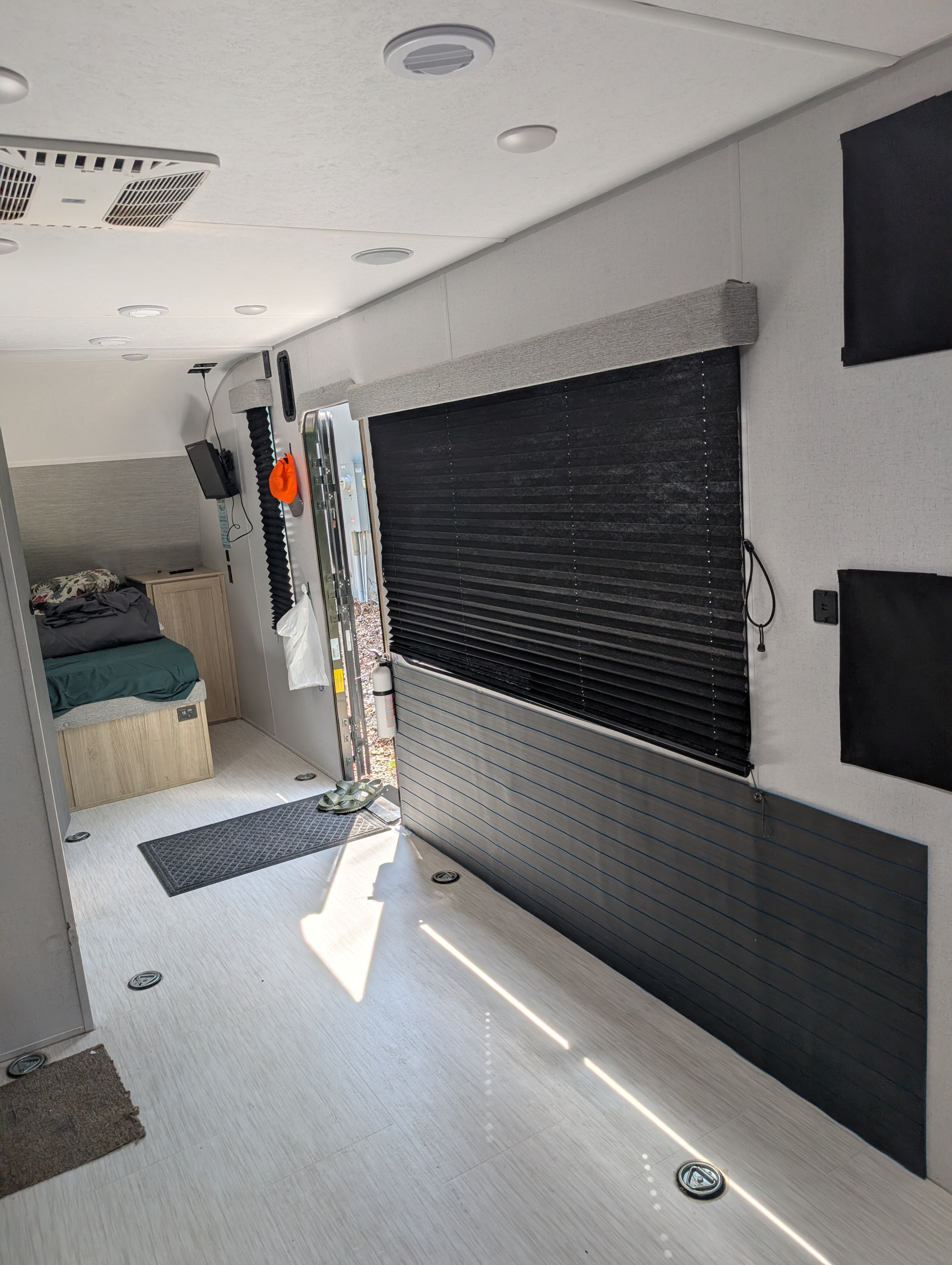 Bright RV rental interior with light plank flooring, ceiling AC, and dark pleated window blinds. Features a rear bunk area and tie-downs.. Forest River Wildwood FSX Platinum Toy Hauler 2023