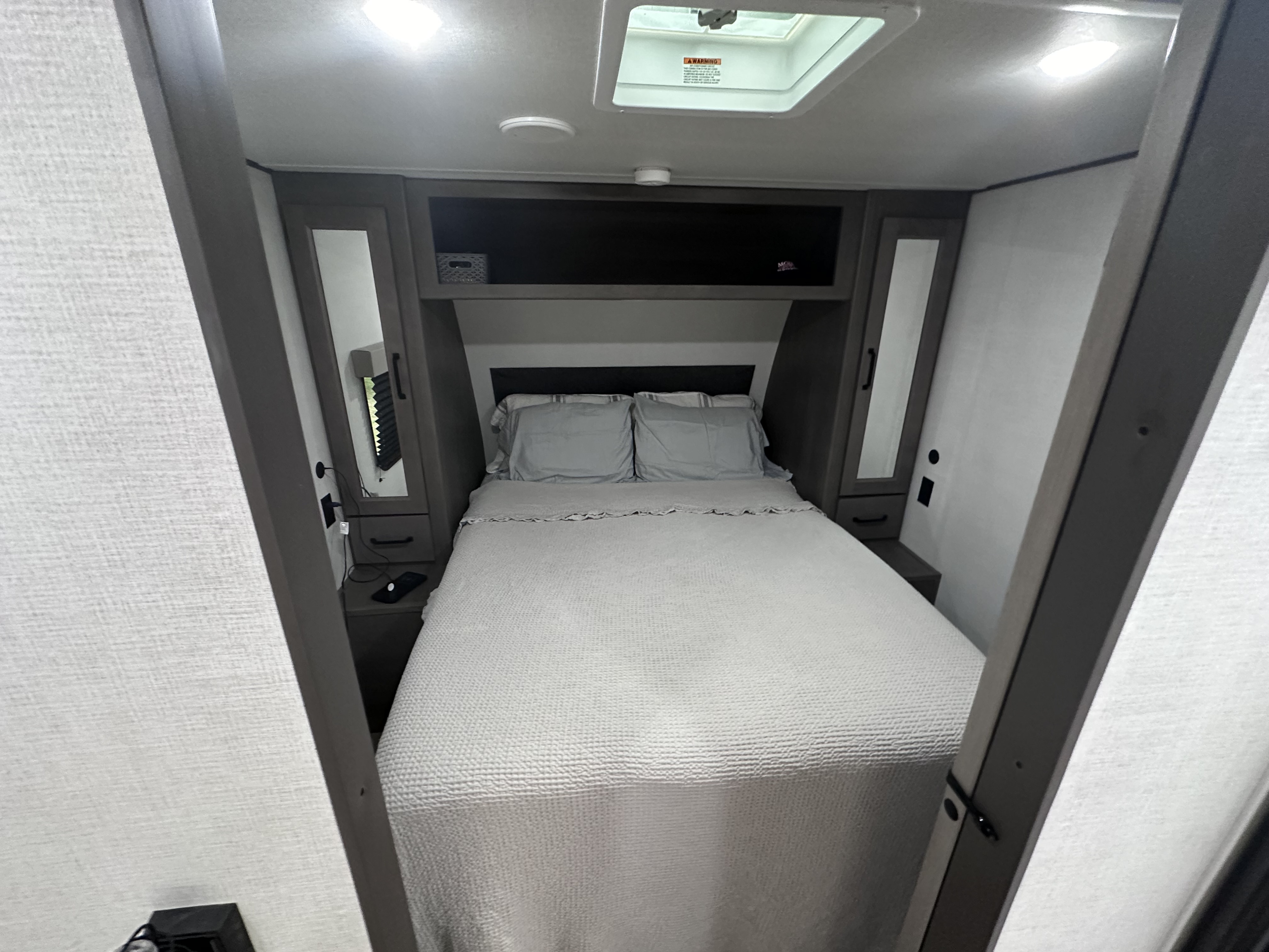 Cozy RV rental bedroom with a comfy bed, overhead storage, and functional bedside cabinets, perfect for travel.. Grand Design Transcend Xplor 2024