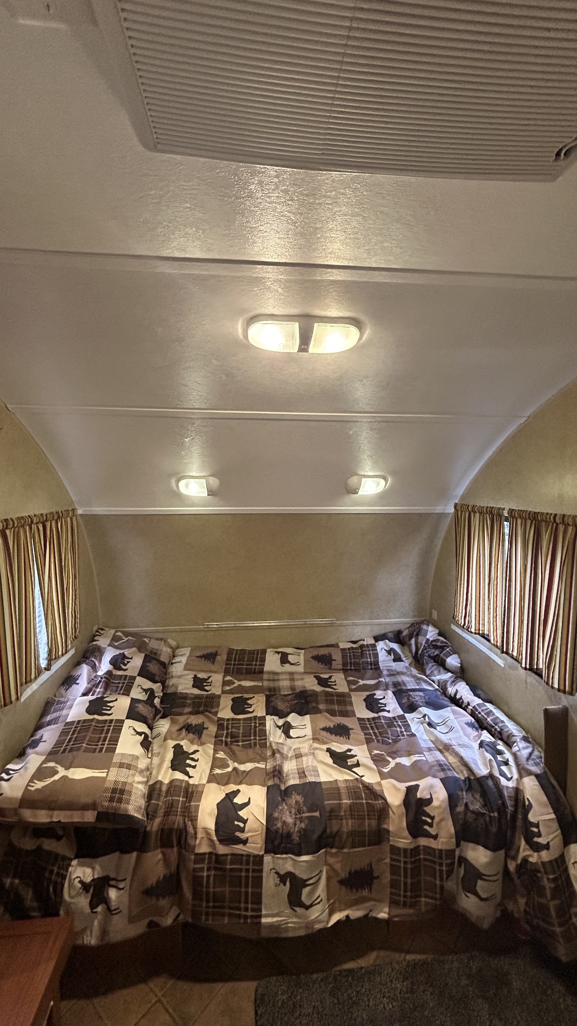Inside an RV rental, a cozy bedroom with a spacious bed, wildlife-themed quilt, striped curtains, and ceiling lights.. R-Pod R-Pod Trailer 2012