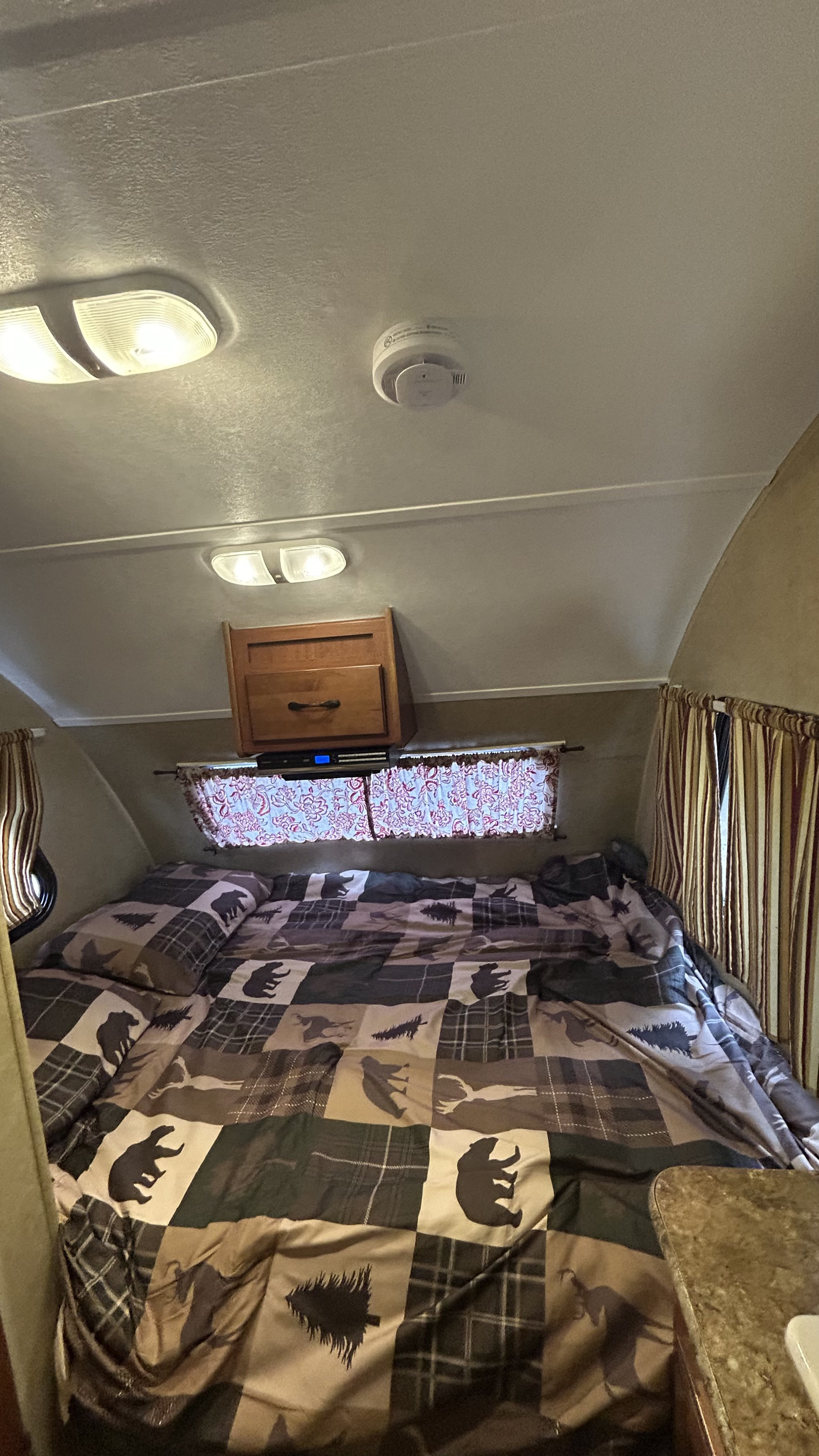 Cozy RV rental bedroom featuring rustic bear-themed bedding, overhead cabinet, window, lights, and smoke detector.. R-Pod R-Pod Trailer 2012