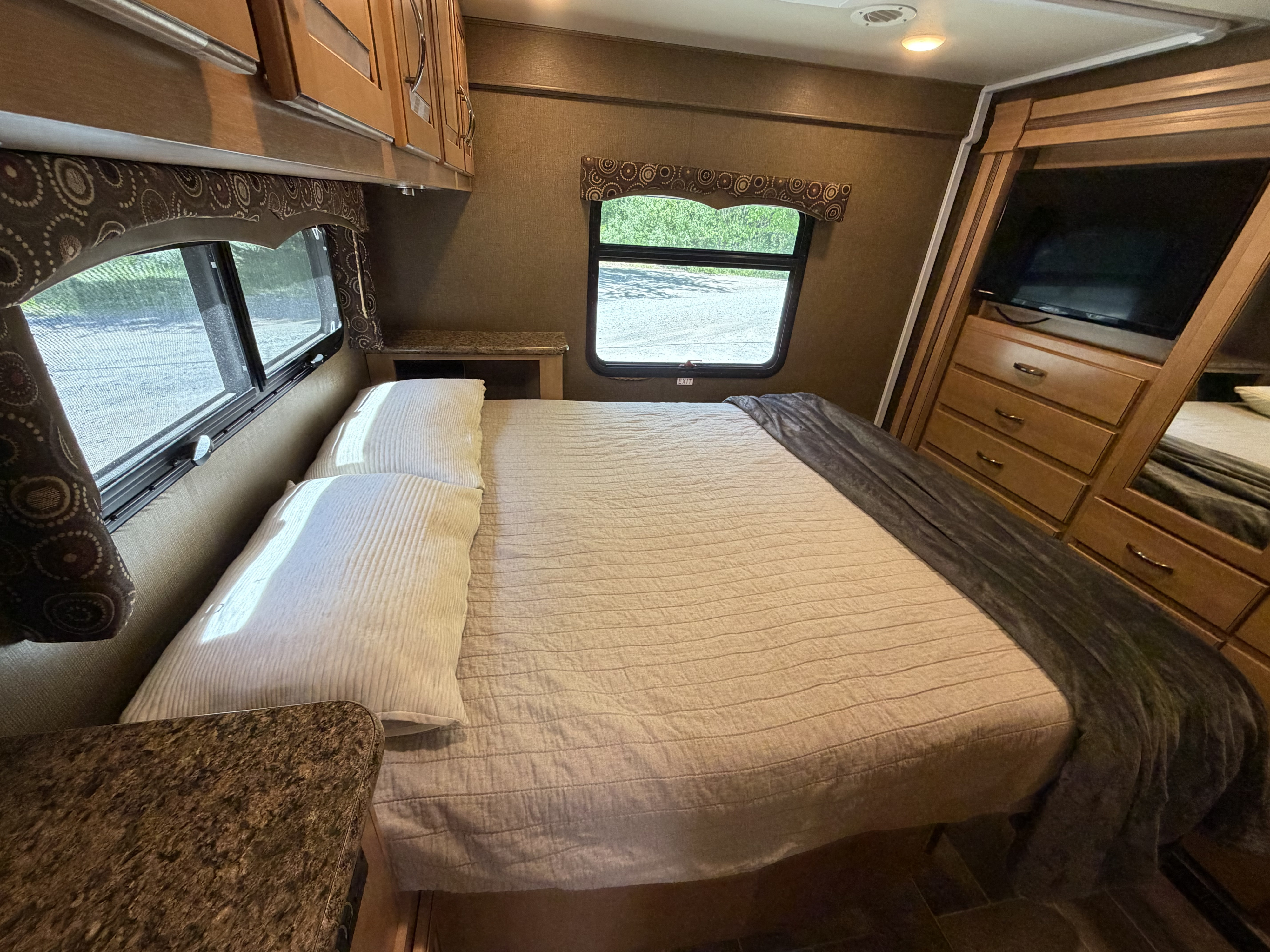 This cozy RV rental bedroom features a comfy bed, windows, built-in storage, and a TV, ensuring a relaxing trip.. Thor Four Winds 2016
