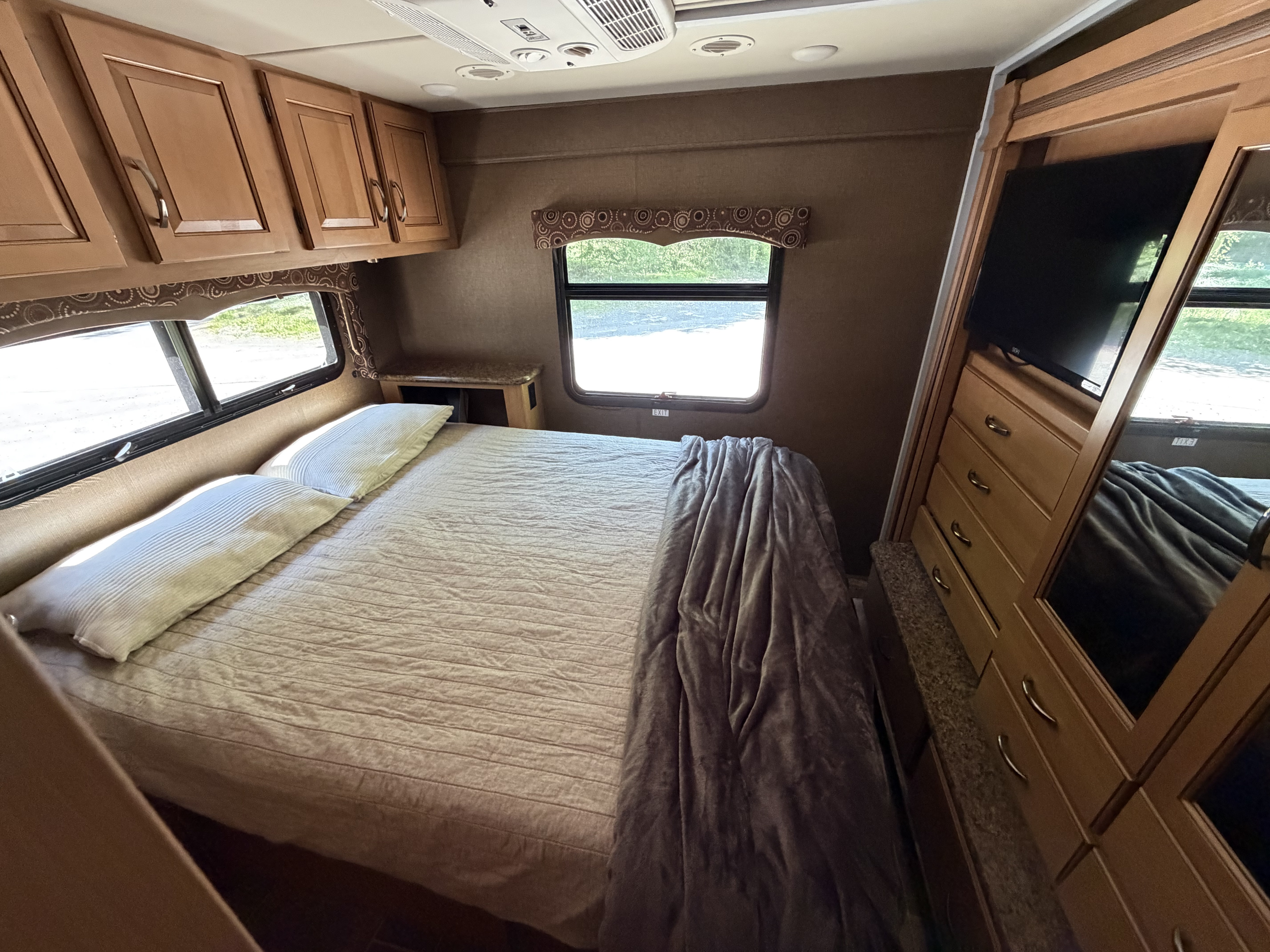 RV rental bedroom interior with a queen bed, overhead cabinets, windows, TV, and dresser. Offers cozy comfort.. Thor Four Winds 2016