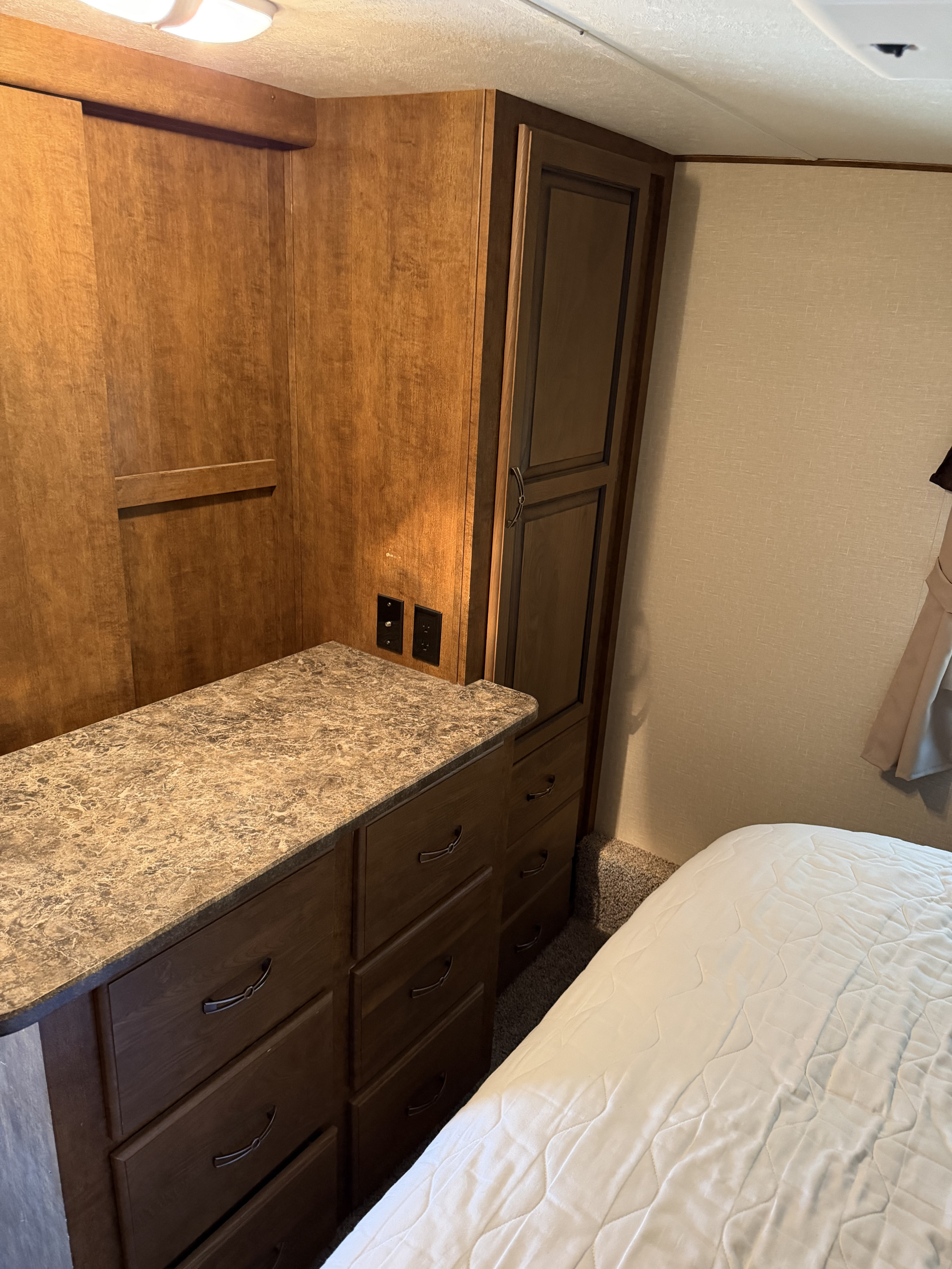 Cozy RV rental bedroom featuring wood-toned cabinetry, a dresser with countertop, and a comfortable bed for restful travel.. Crossroads RV Rezerve 2015