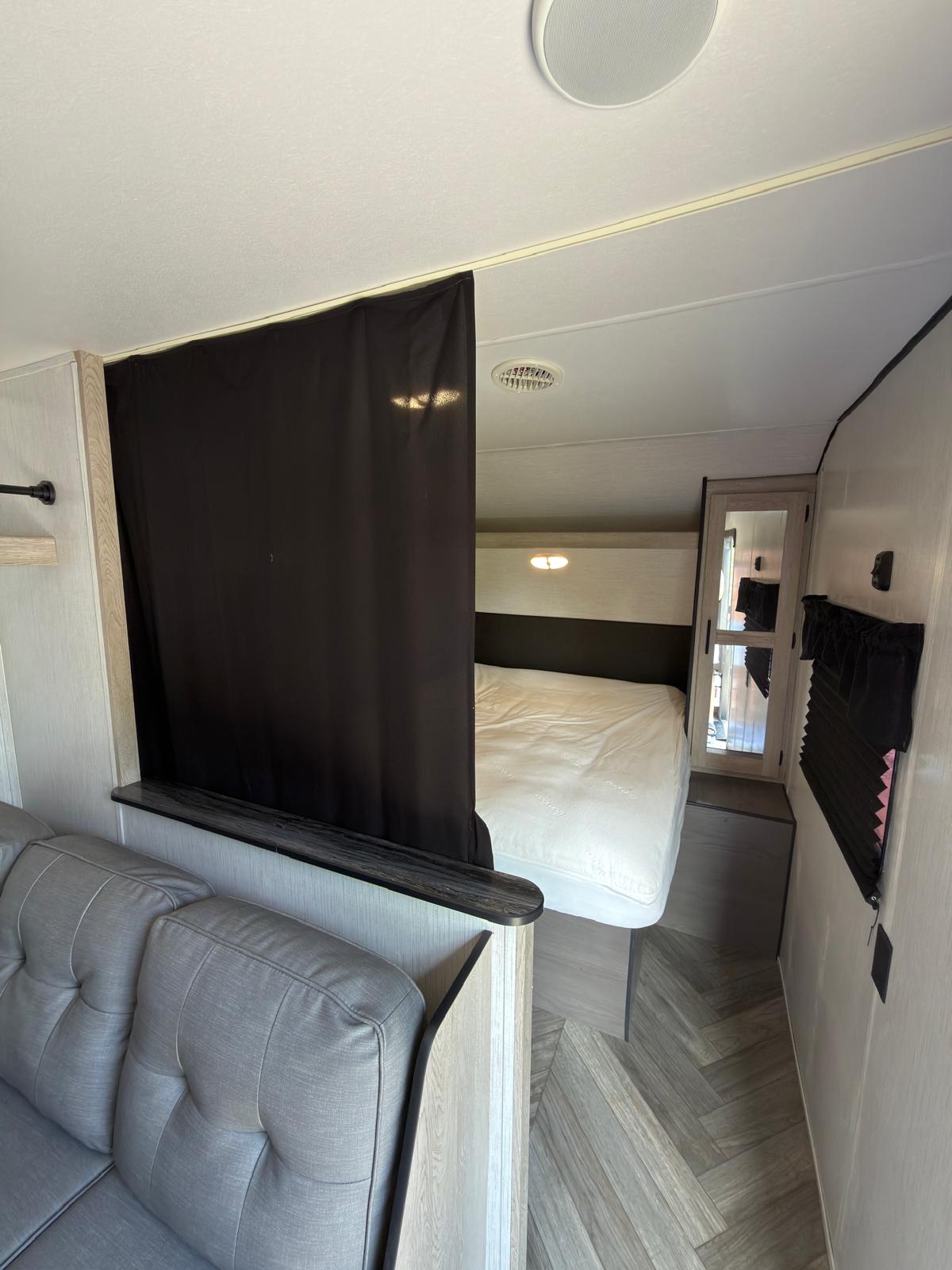 Inside a modern RV rental: a compact living area with a sofa and a private bedroom separated by a curtain. Note the stylish floor.. Heartland RVs Prowler 2022