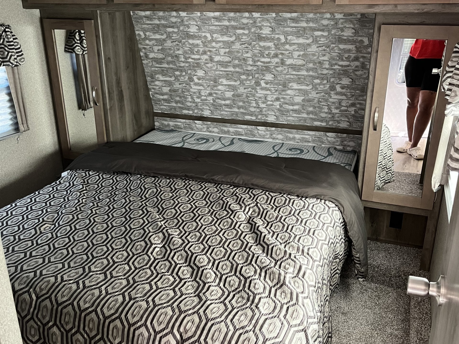 Cozy RV rental bedroom featuring a comfy bed with geometric bedding, brick accent wall, and mirrored closet doors.. Keystone RV Sprinter Campfire Edition 2019