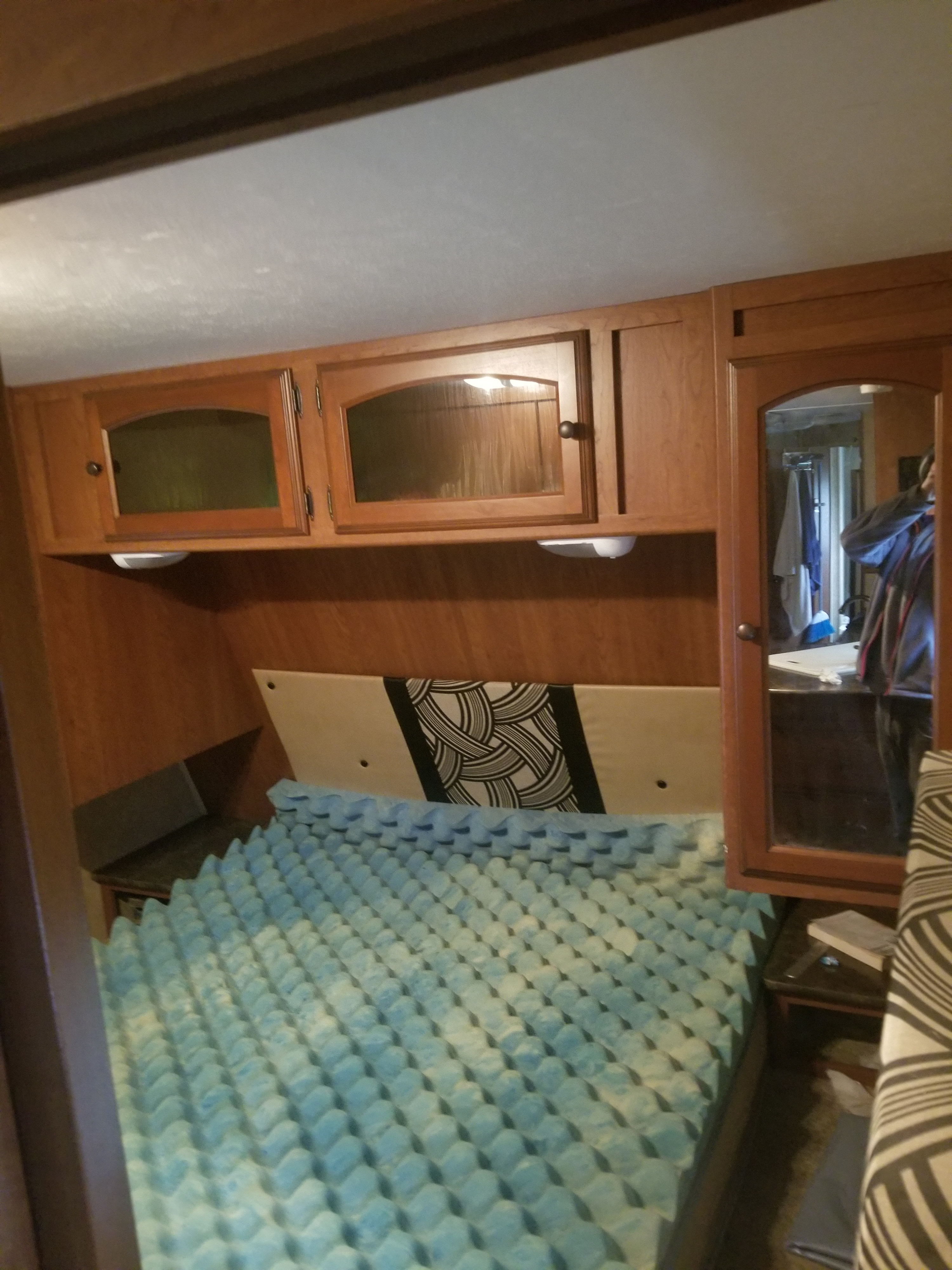 RV rental bedroom featuring a blue egg crate mattress topper, overhead wooden cabinets, and mirrored closet door.. Dutchmen Dutchmen Trailer 2014