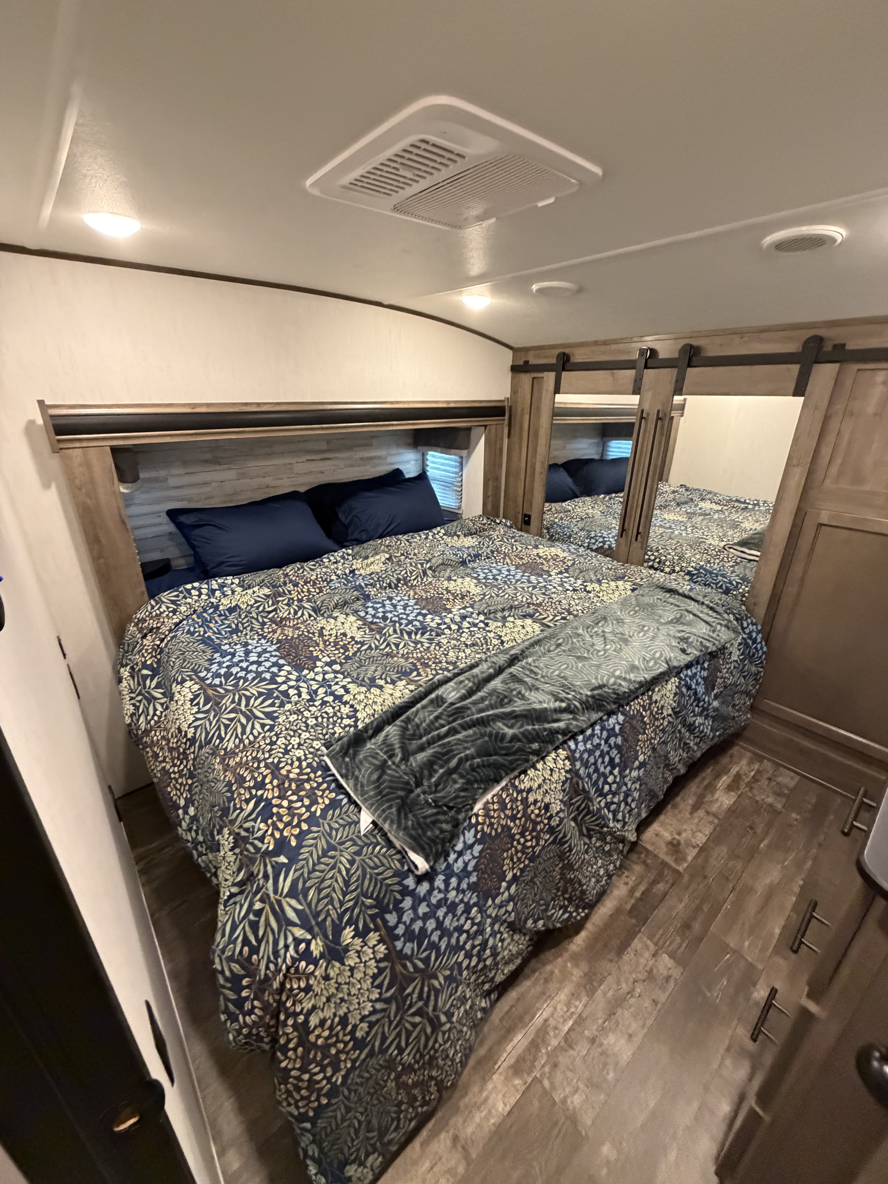 Cozy RV rental bedroom with patterned bedding, mirrored closets, ceiling AC unit, and wood floors for a comfortable stay.. Forest River Sabre 2022