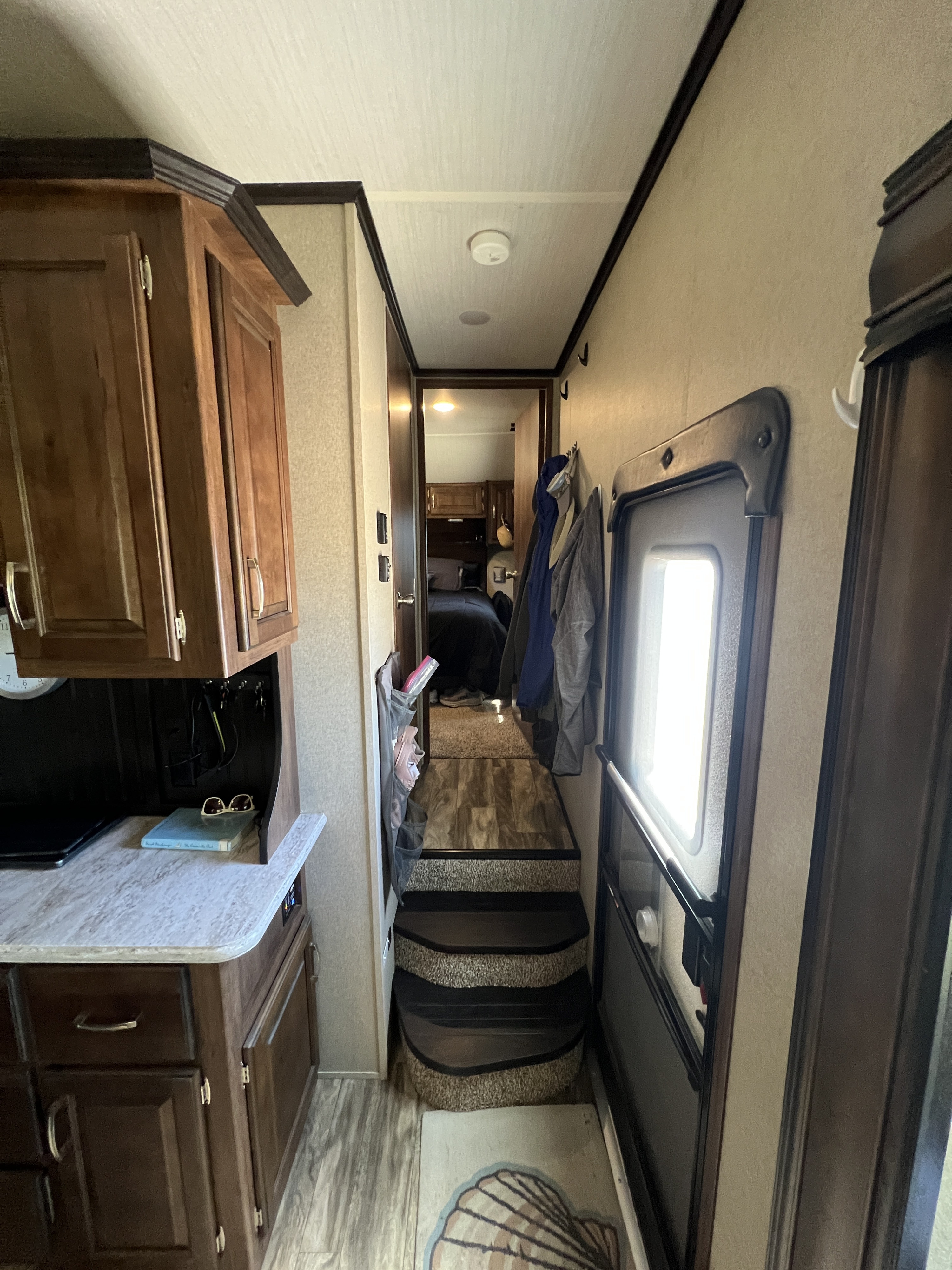Warm-toned RV rental interior with dark wood cabinets, steps to bedroom, and a bright main entrance.. Grand Design Reflection 2019