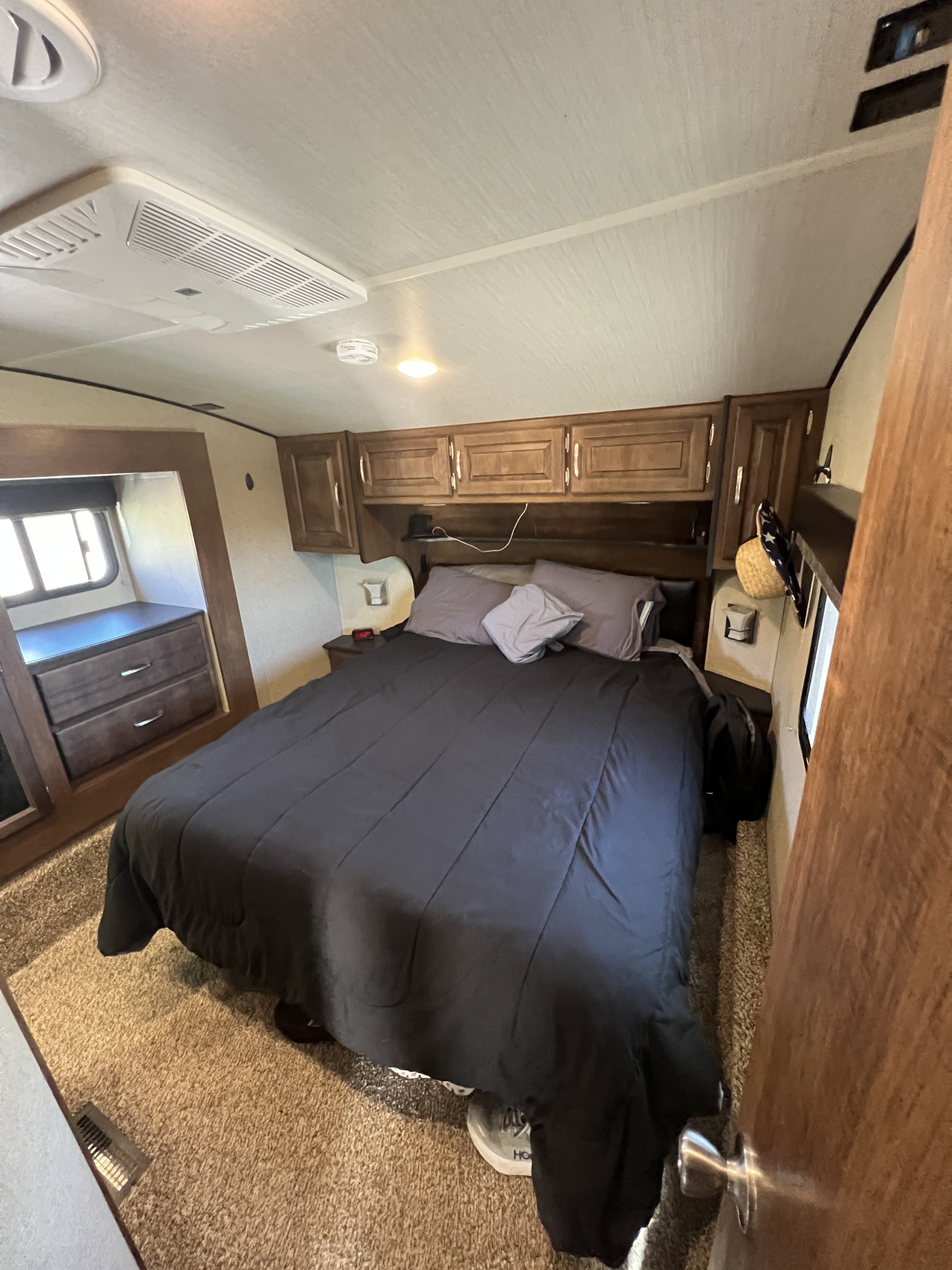 Cozy RV rental bedroom with a queen bed, dark bedding, wooden storage cabinets, and ceiling AC unit. Ideal for your next trip.. Grand Design Reflection 2019