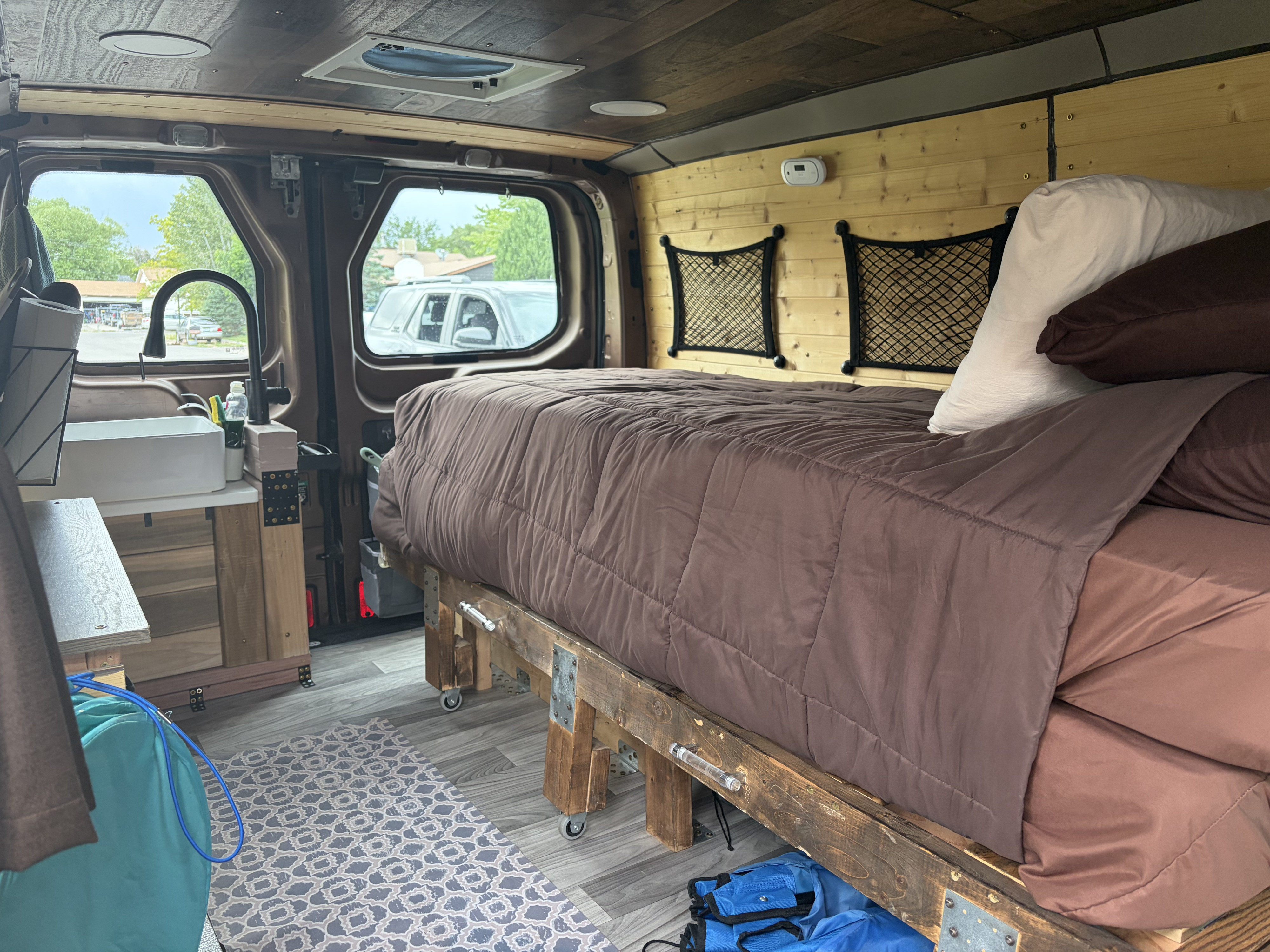 Cozy RV rental interior with a comfy bed, kitchenette, and wood paneling. Perfect for van life adventures!. FORD TRANSIT 250 2015