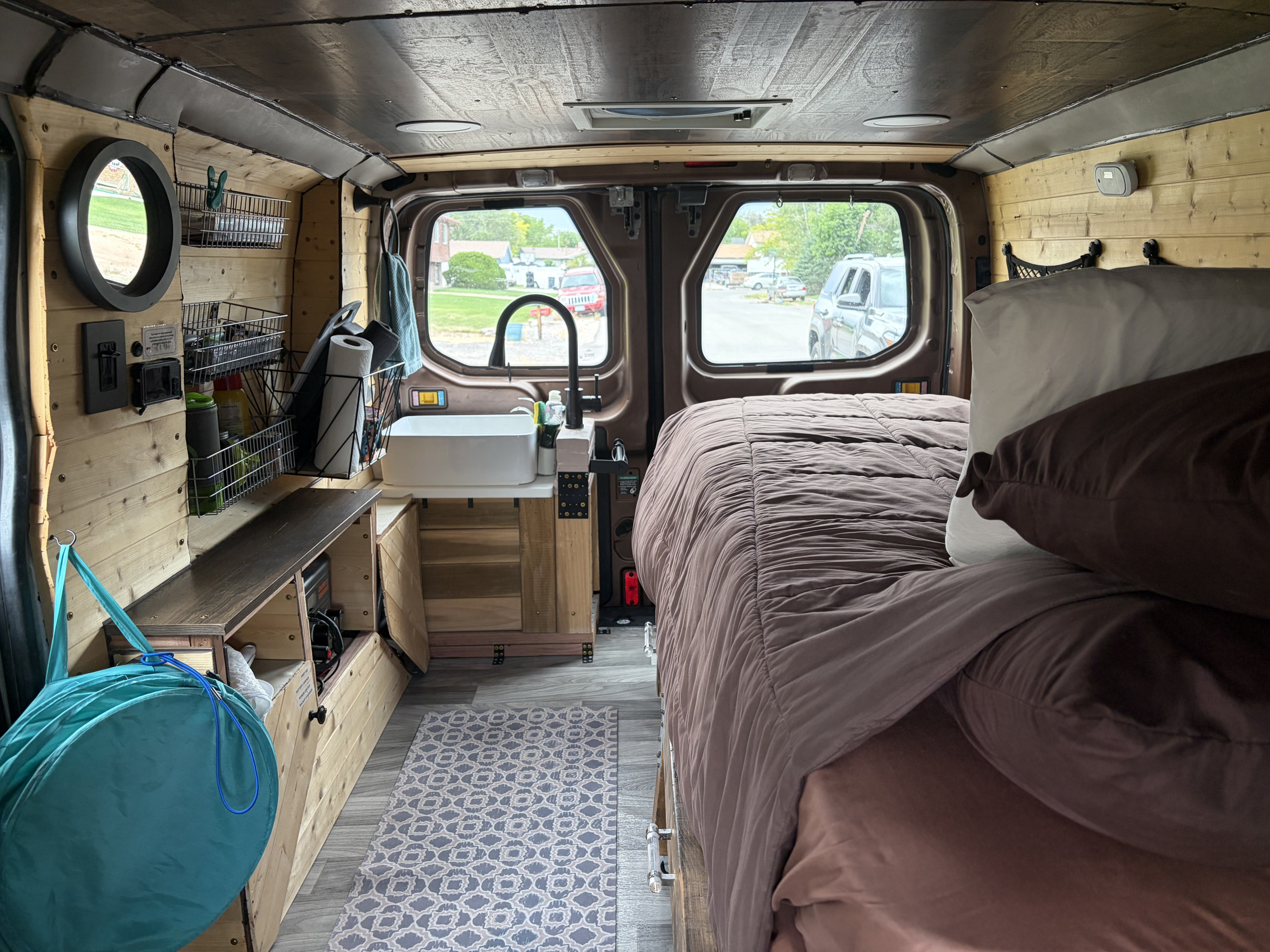 Cozy rv rental camper van interior features a bed, kitchen area with sink, wooden walls, and patterned rug for mobile living.. FORD TRANSIT 250 2015