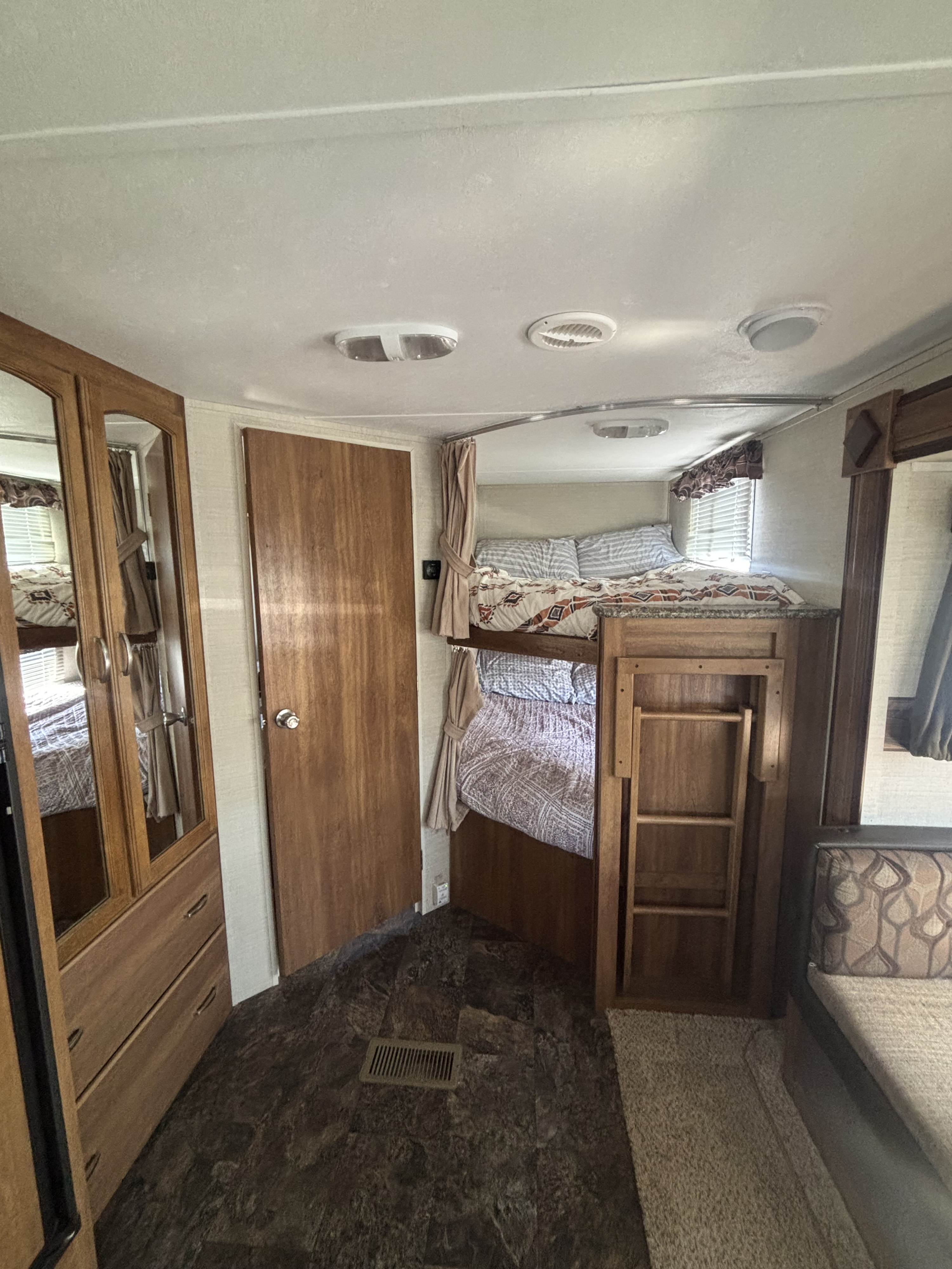 RV rental interior: two bunk beds with patterned bedding and a ladder, a tall wooden wardrobe with mirrors, and a small sofa.. Keystone RV Springdale 2015