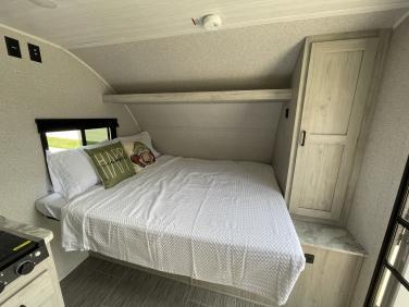 Explore this inviting RV rental bedroom with a comfy bed, overhead shelf, and wardrobe, ideal for comfortable travel.. East to West Silver Lake 2023