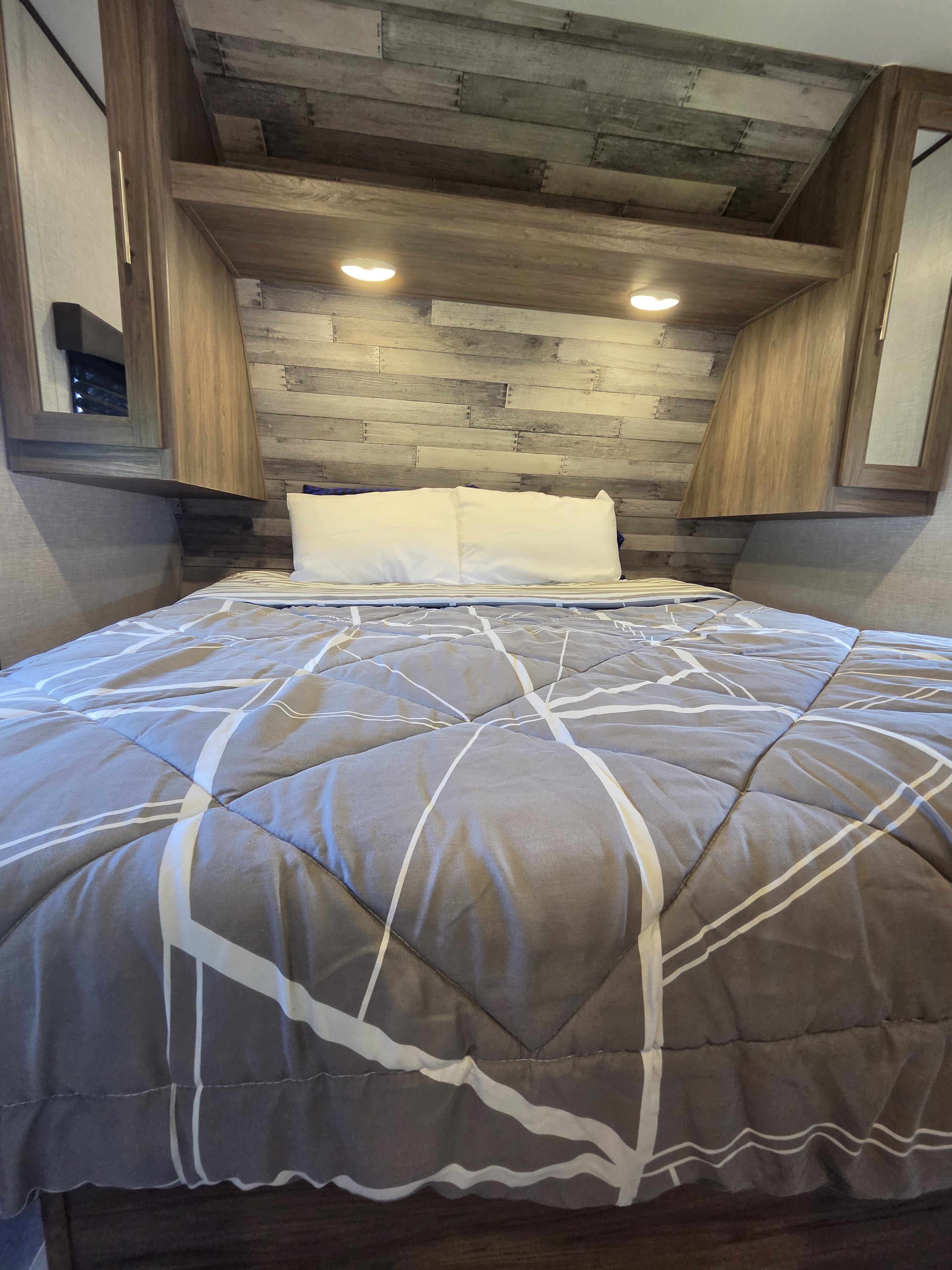 Cozy RV rental bedroom with a comfortable bed, gray geometric comforter, white pillows, wood paneling, and warm lighting.. Crossroads RV Zinger 2021
