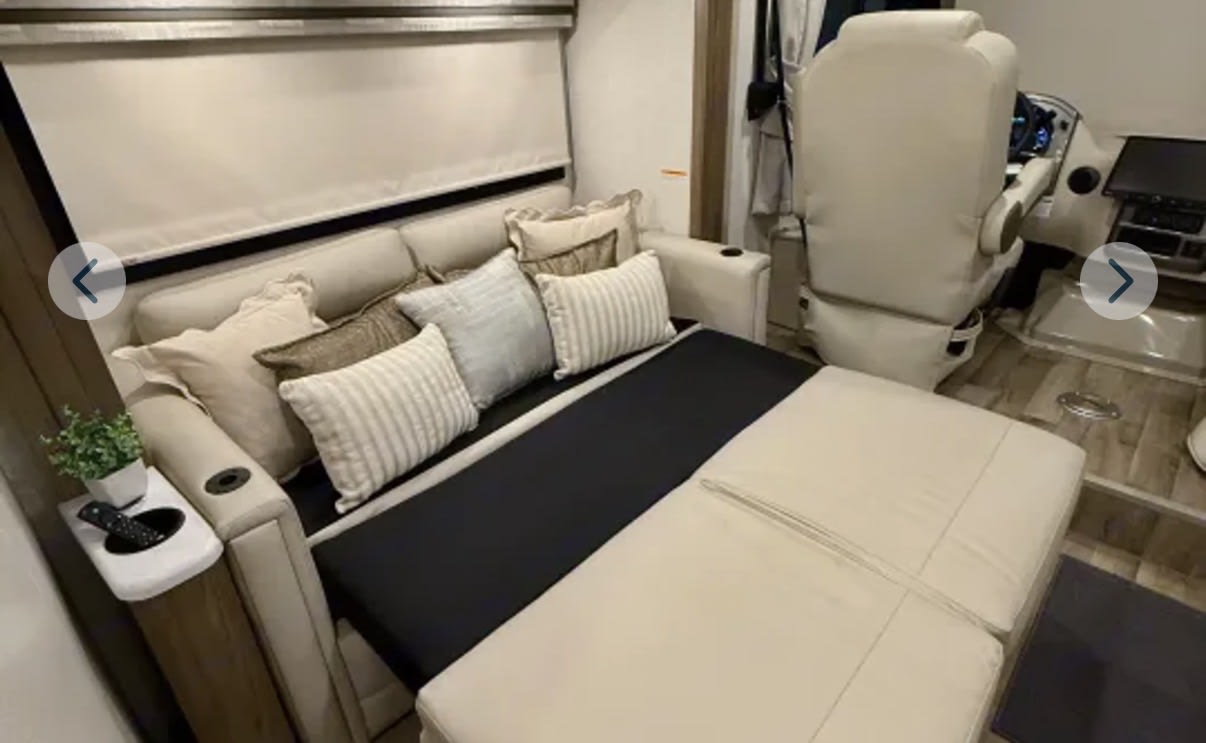 RV rental: Motorhome living area with a sofa converted to a bed, showing cream upholstery and the driver's seat beyond.. Thor Motor Coach Vegas 2026