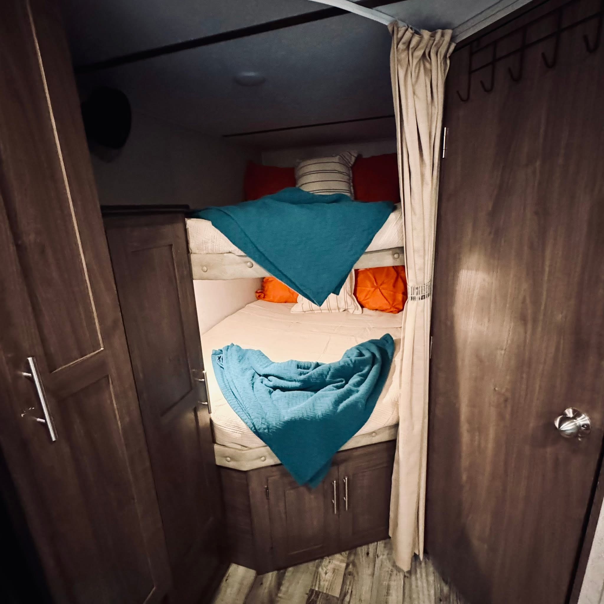 This RV rental offers cozy bunk beds with teal blankets & pillows, set in dark wood cabinetry. Ideal compact sleeping space.. Keystone RV Hideout LHS 2019