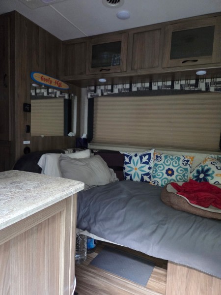 Inside an RV rental, a comfy bed with decorative pillows and overhead storage cabinets, perfect for travel comfort.. Coachmen Freelander 2016
