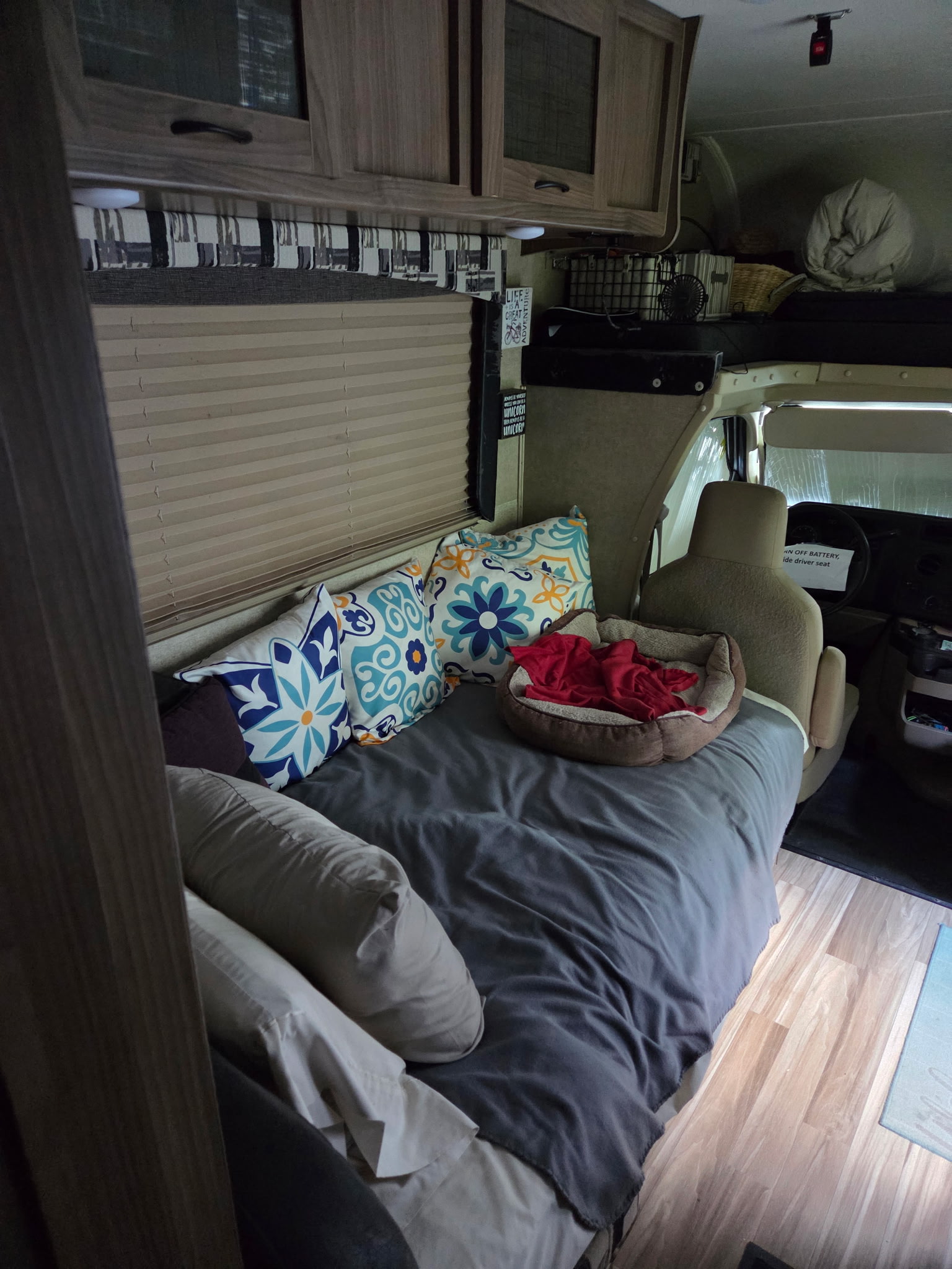 Cozy RV rental interior featuring a made-up bed with decorative pillows, a pet bed, and a visible driver's seat.. Coachmen Freelander 2016