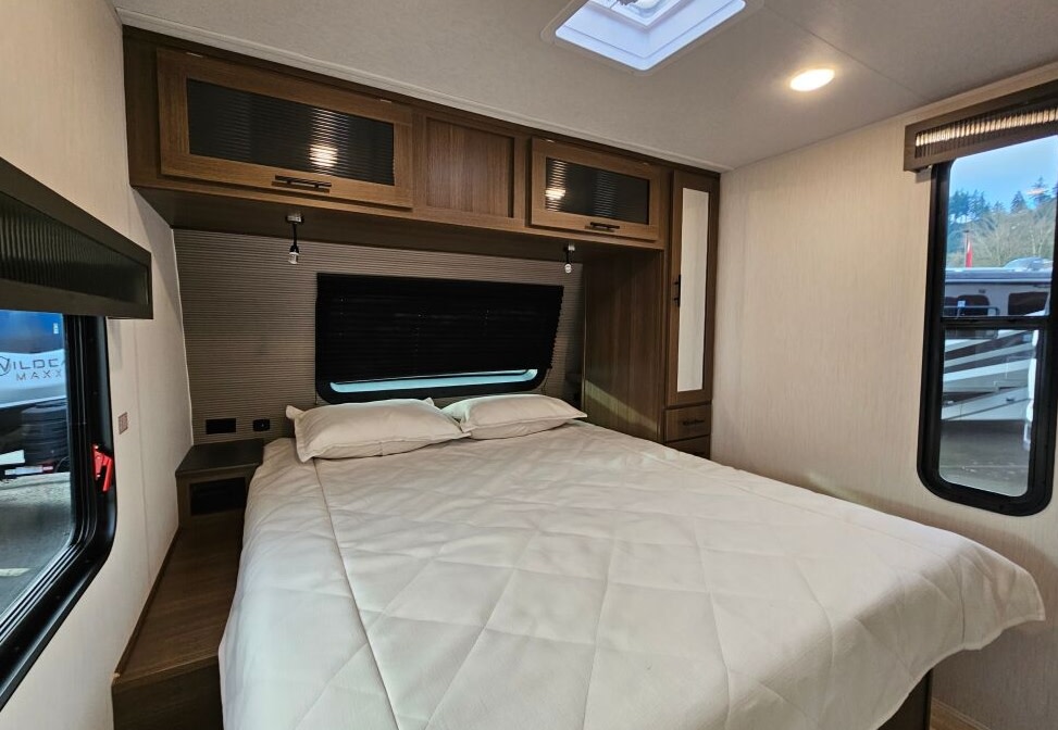 Cozy RV rental bedroom with white bed, overhead cabinets, and large window. Features storage & bright interior.. Forest River 246DBX 2026
