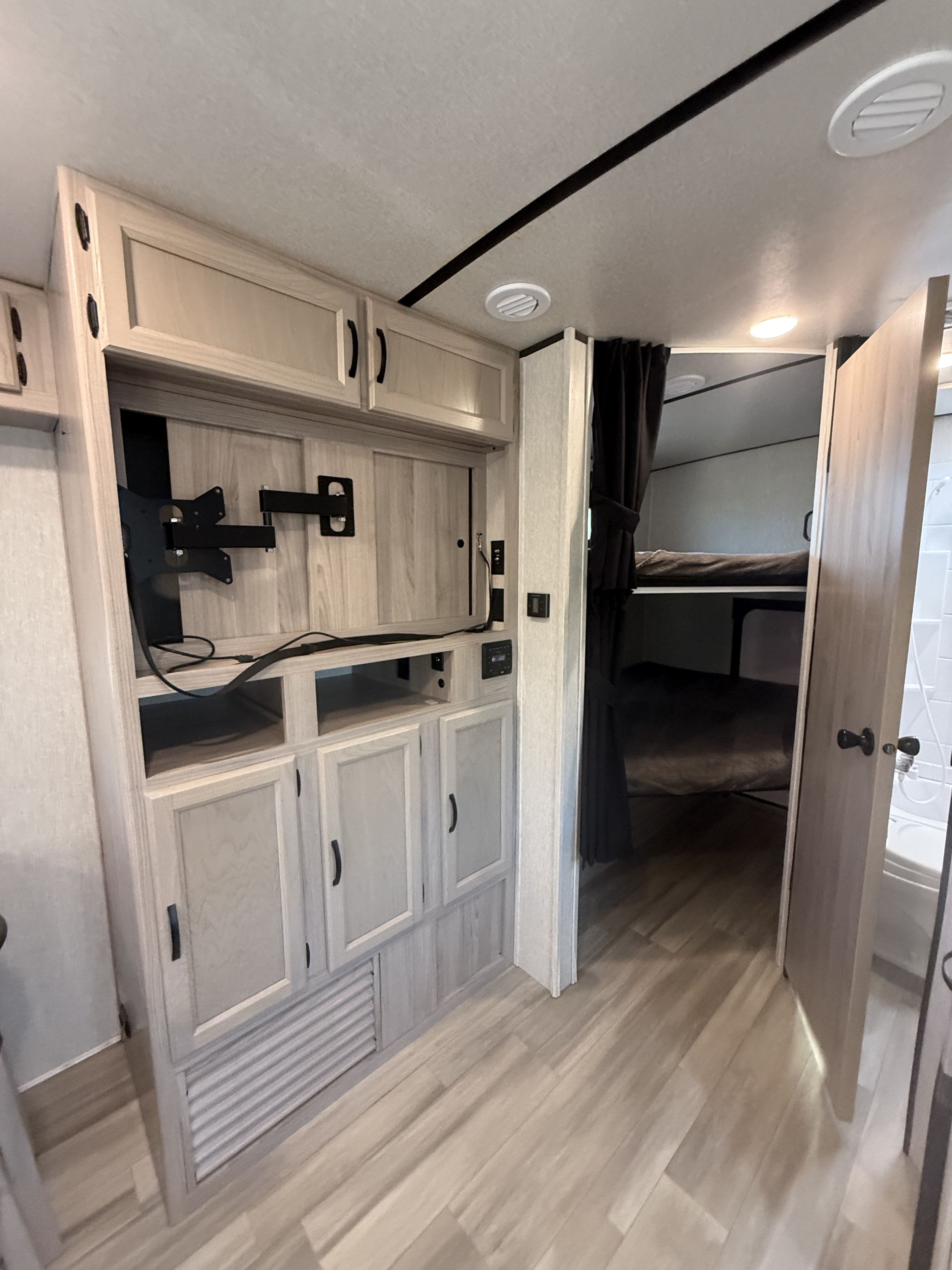 Modern RV rental interior with a light wood entertainment unit, overhead storage, bunk beds on the right, and a compact bathroom.. Spirit Ultralite 2659BH 2021