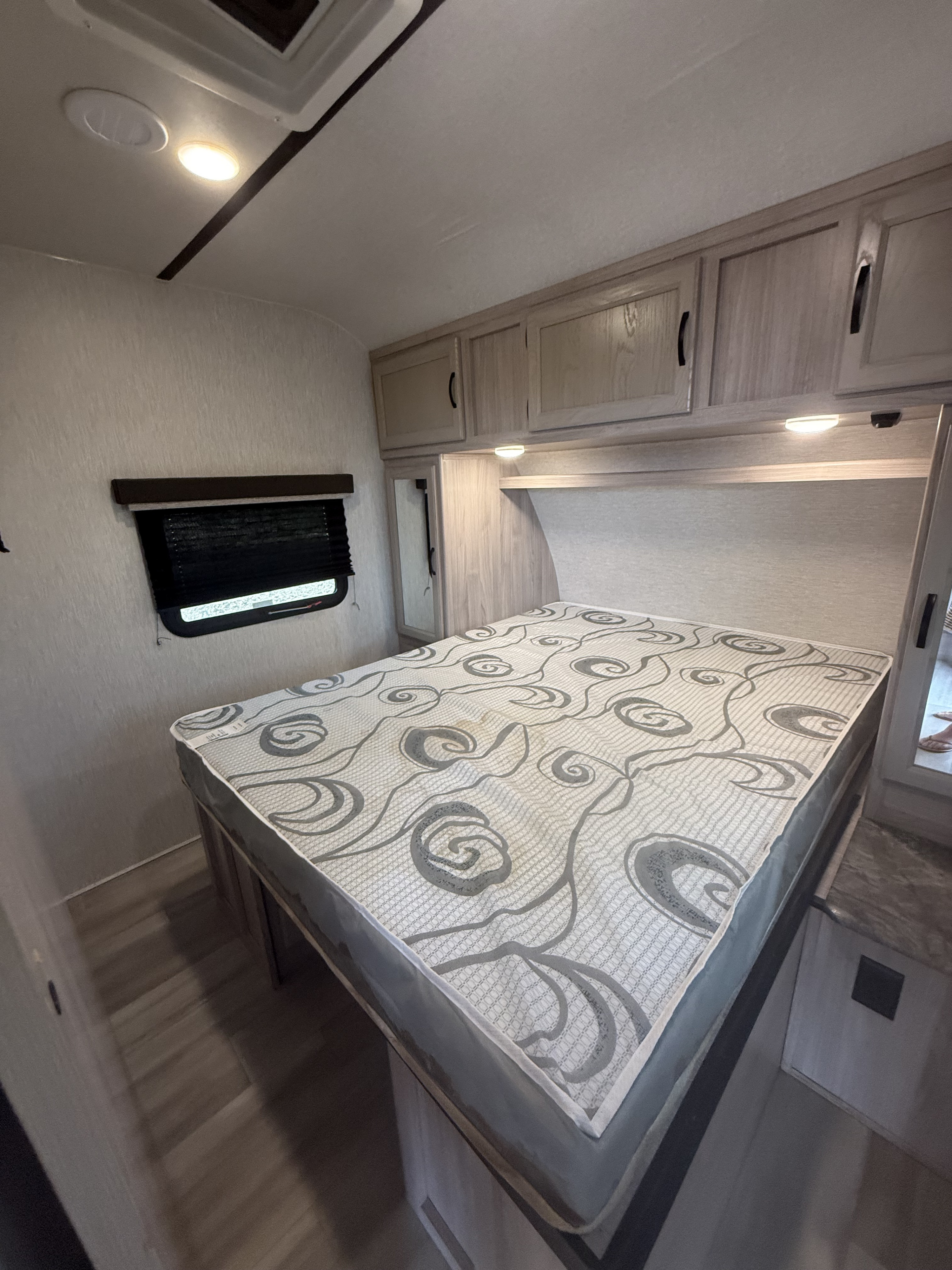 Spacious RV rental bedroom with a patterned mattress, overhead cabinets, a window with blinds, and light wood accents.. Spirit Ultralite 2659BH 2021