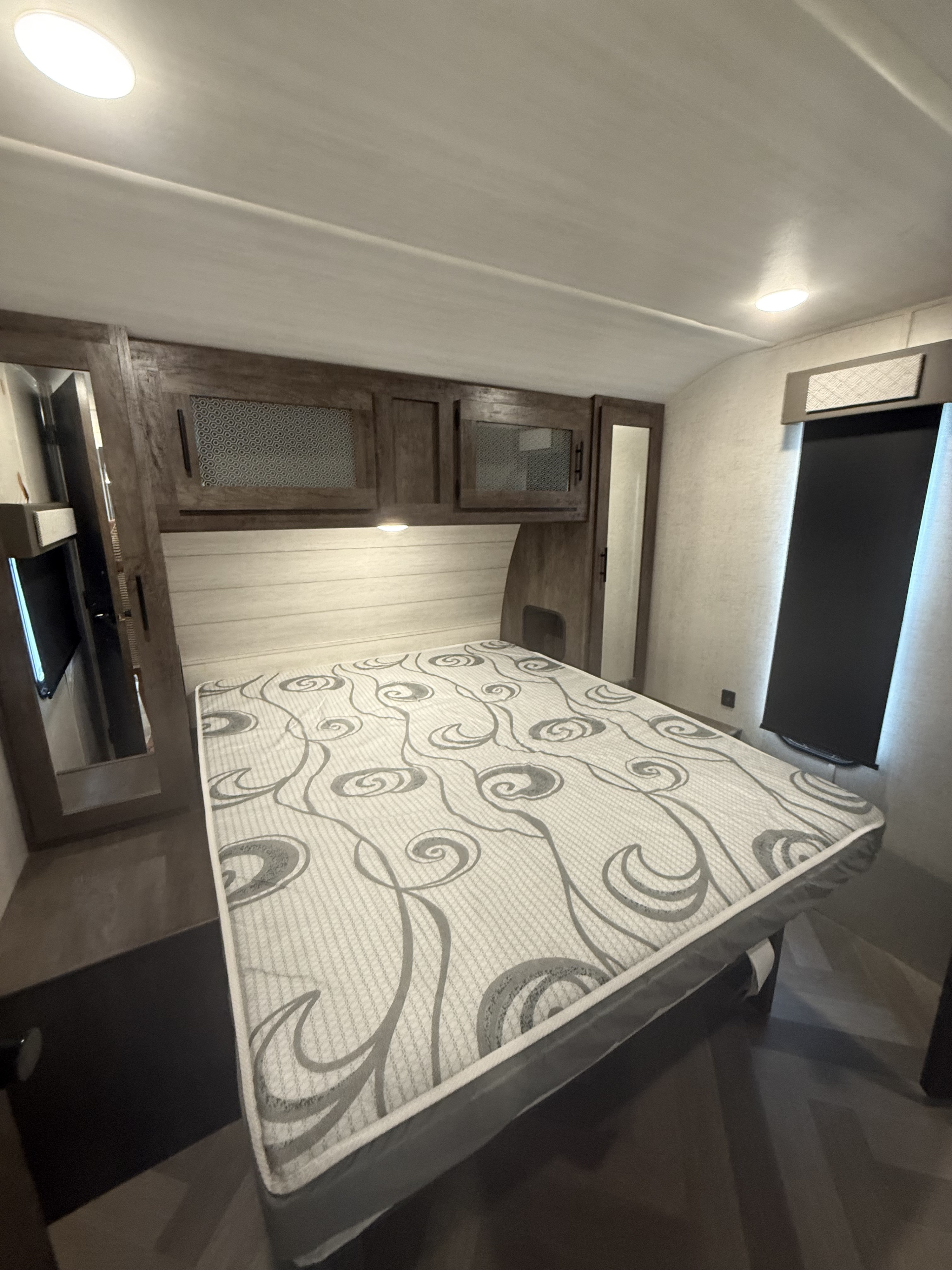 RV rental bedroom with patterned mattress, wood overhead cabinets, and built-in mirrors, showcasing a compact sleeping area.. Forest River Salem 2021