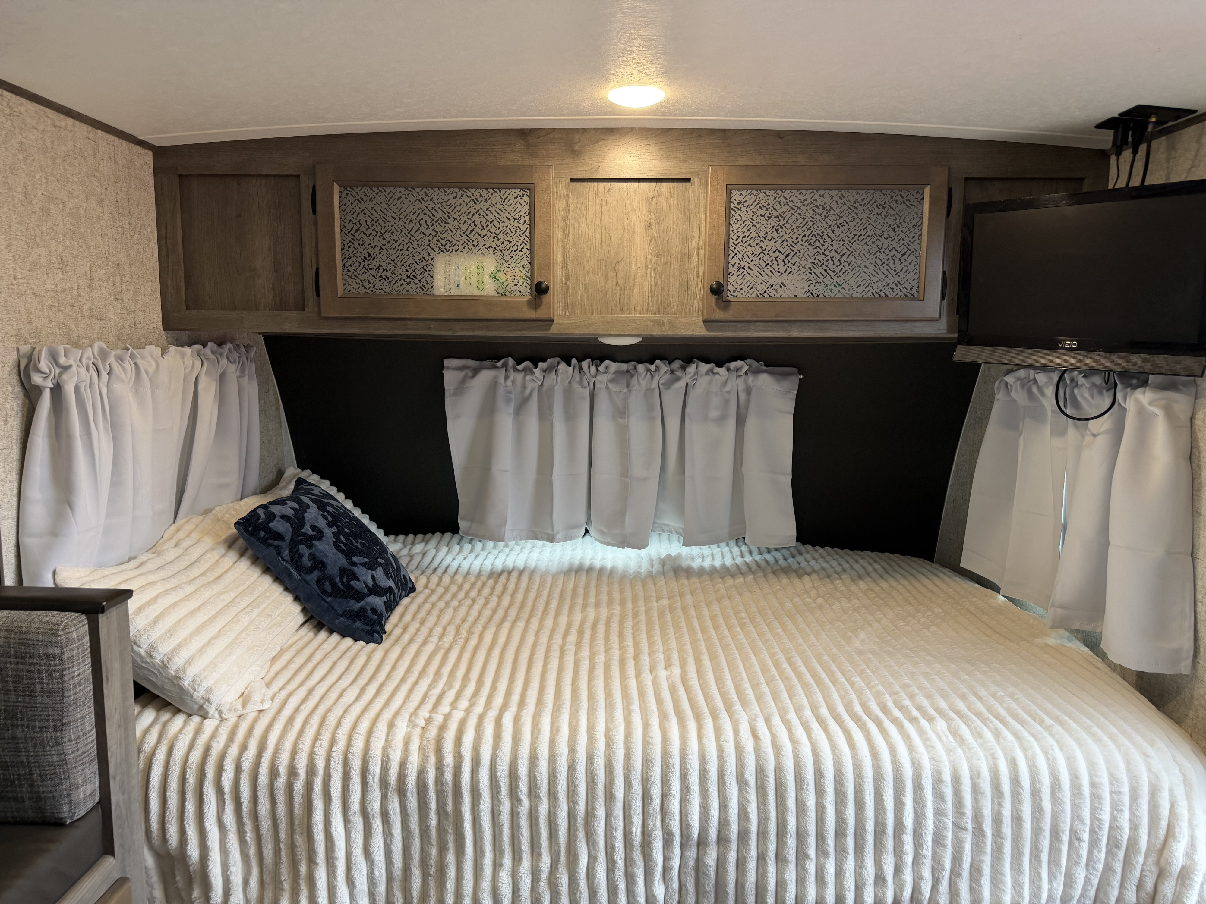 Cozy RV rental bedroom featuring a large bed, wood cabinets, and a TV for comfortable travels.. Coachmen Apex Nano 2022