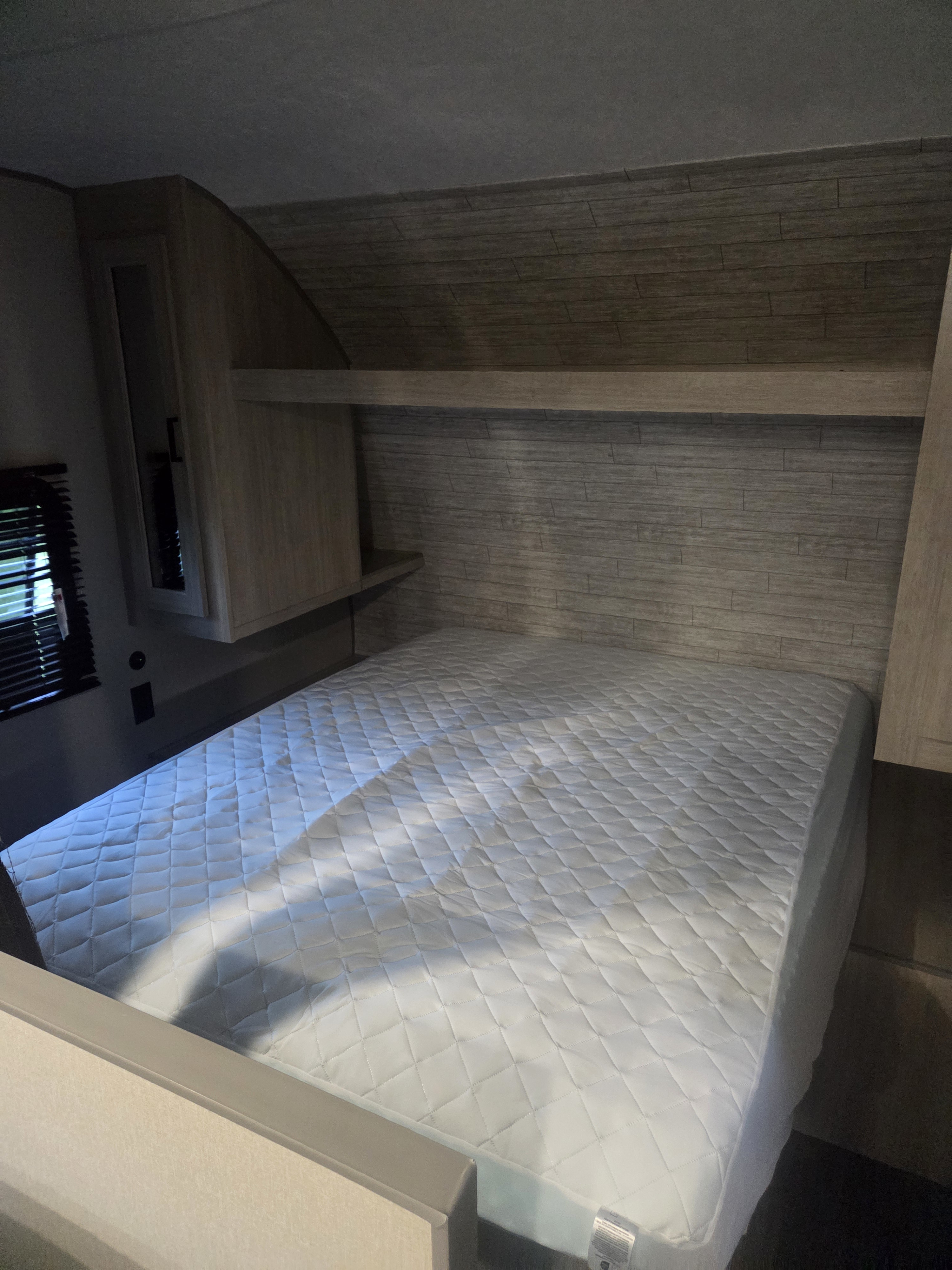 RV rental bedroom featuring a comfy bed with quilted mattress, overhead cabinets, and wood-paneled walls.. Forest River Aurora Aurora 2026