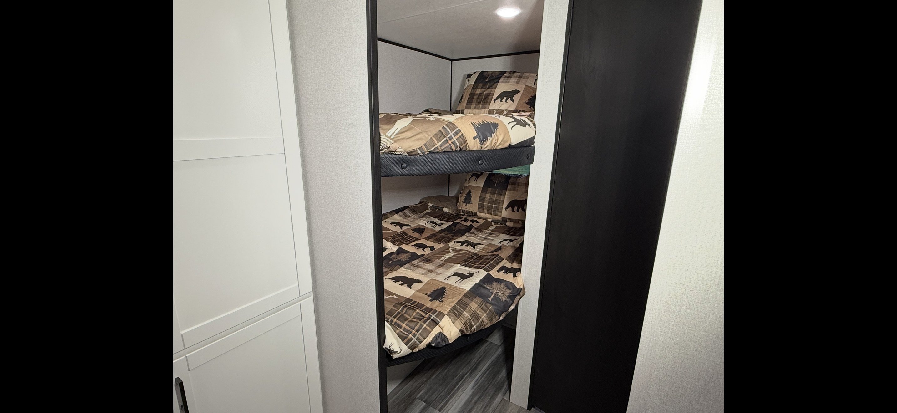 An RV rental interior shows two cozy bunk beds with rustic plaid bedding featuring bears and trees.. Jayco Jay Flight SLX 261BHS 2026