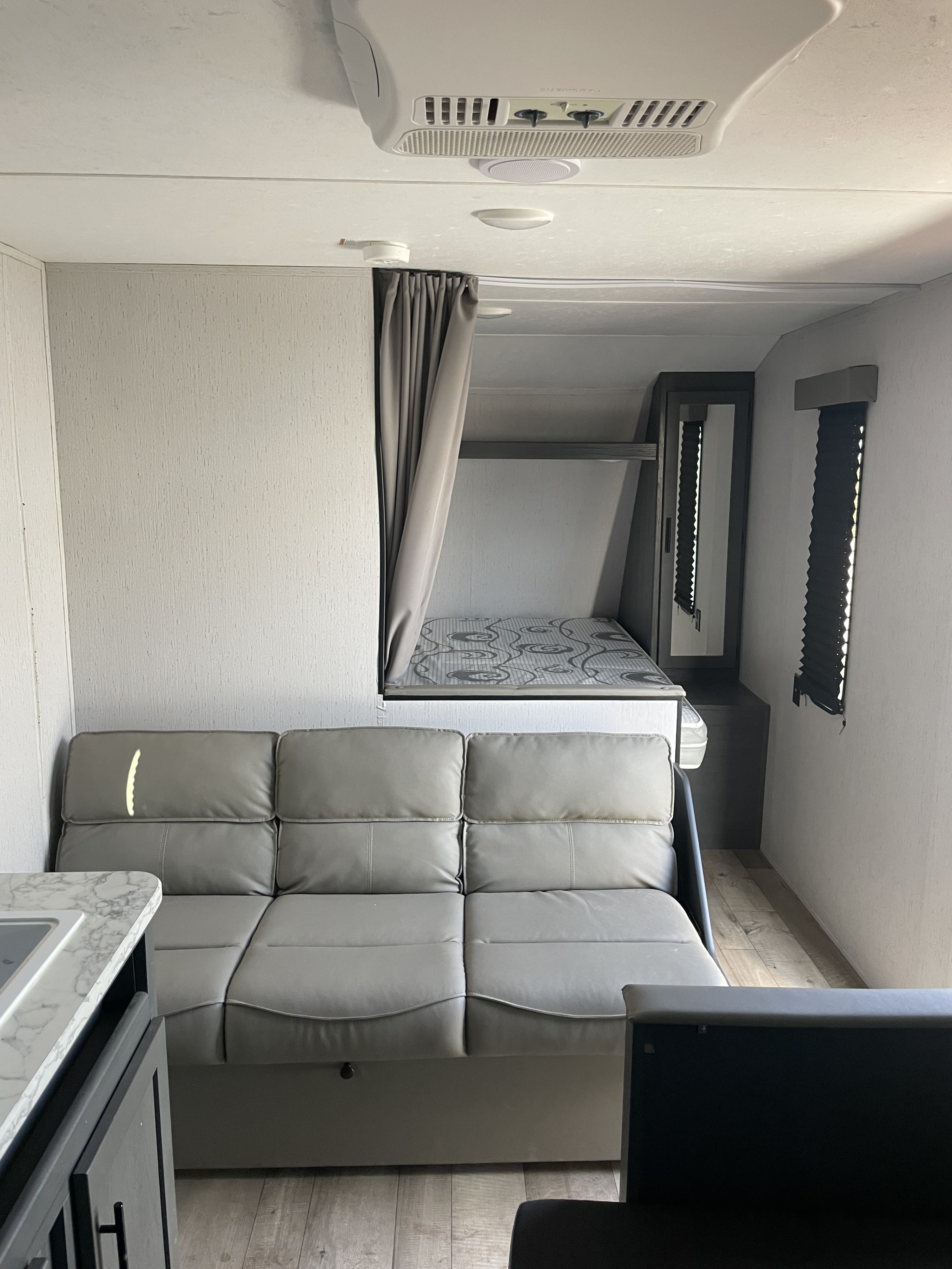 Spacious rv rental interior featuring a cozy gray sofa, upper bunk bed, and compact kitchenette for comfortable travel.. Aspen Trail LE 2022