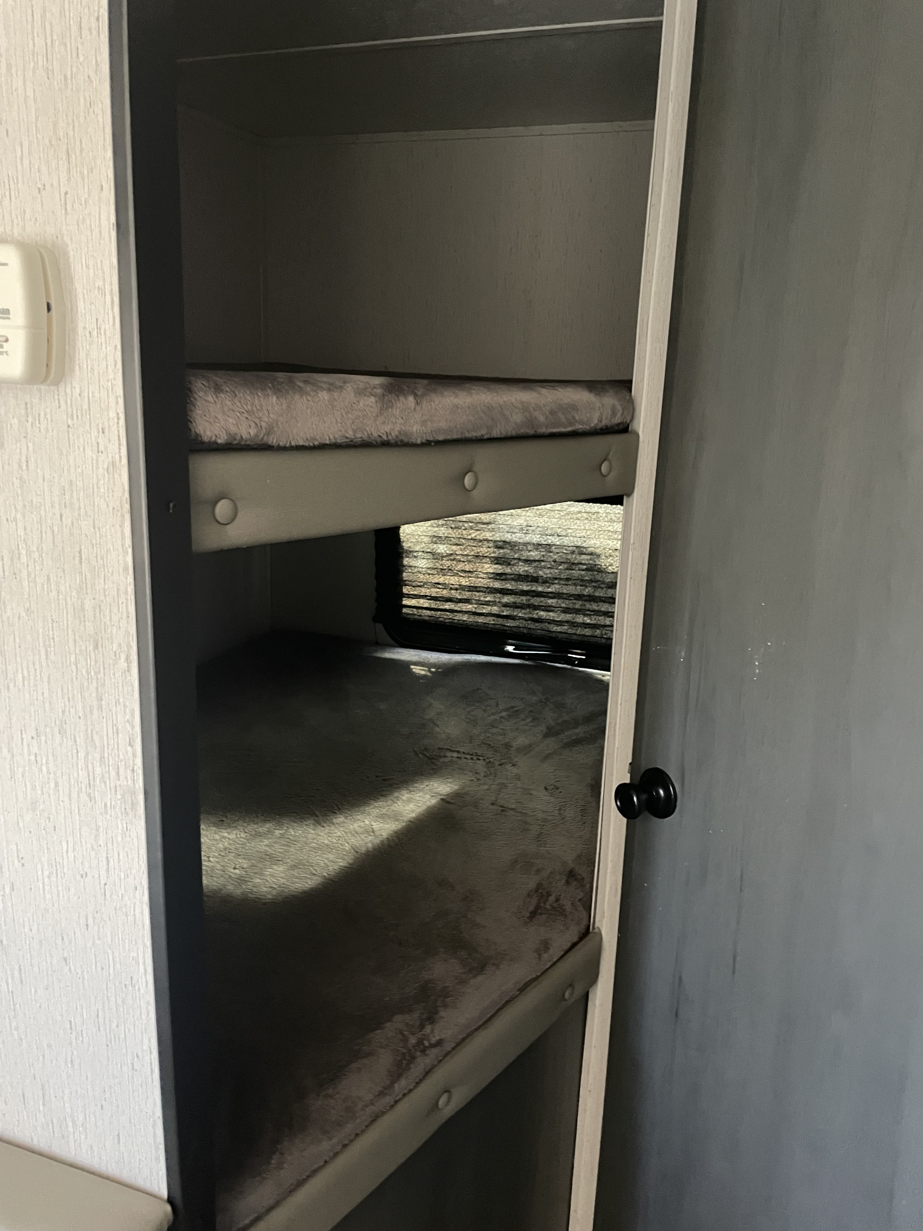 Cozy bunk beds in an RV rental, featuring grey mattresses, a window with blinds, and compact sleeping for travelers.. Aspen Trail LE 2022
