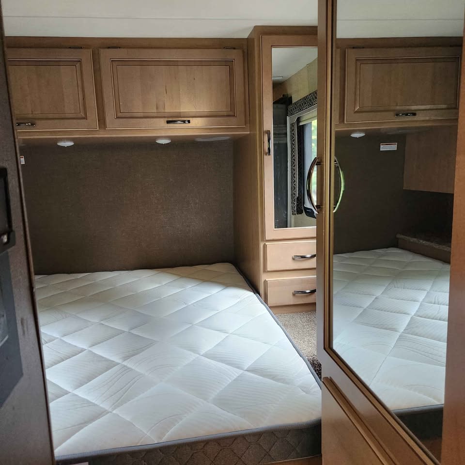 RV rental bedroom with a comfortable white mattress, overhead storage cabinets, and a mirrored wardrobe, perfect for travel.. Thor Four Winds 2018