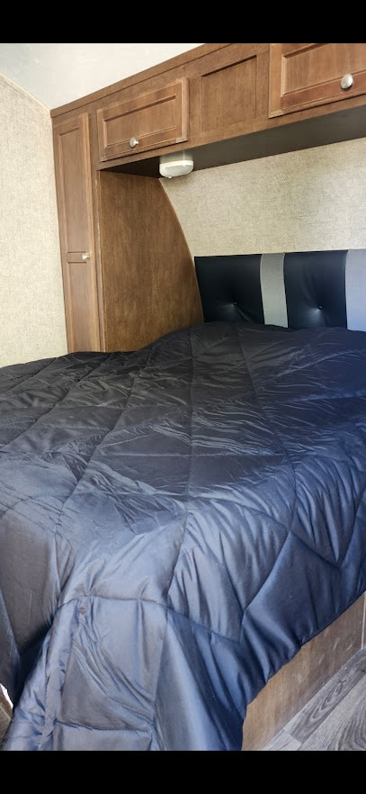 Cozy RV rental bedroom with dark comforter, striped headboard, and wooden cabinets. Perfect for your next adventure.. Sonic Sonic Trailer 2019
