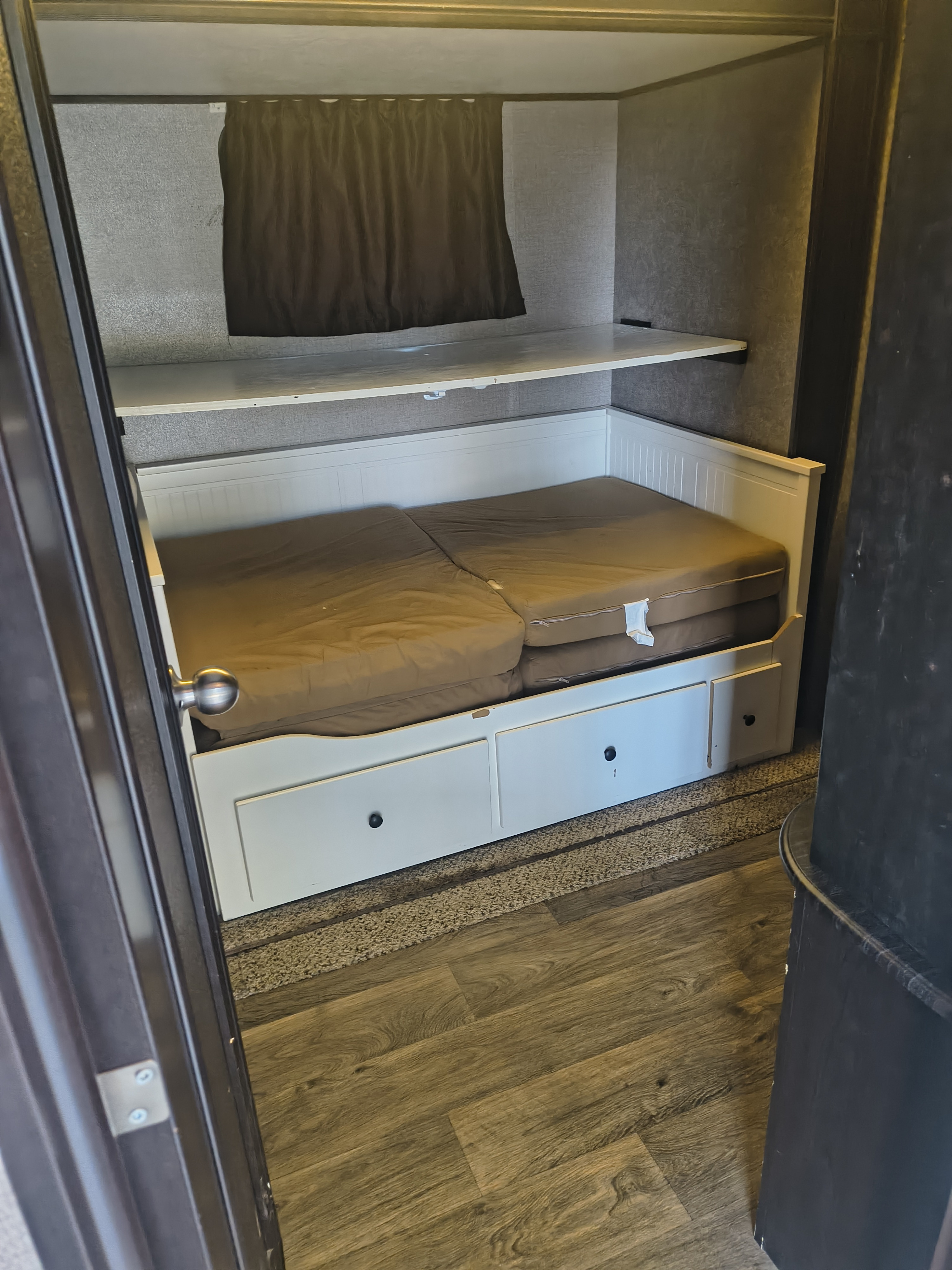 RV rental bunk area: a white bunk bed with storage drawers, an upper shelf, and a dark privacy curtain.. Jayco Eagle 2019