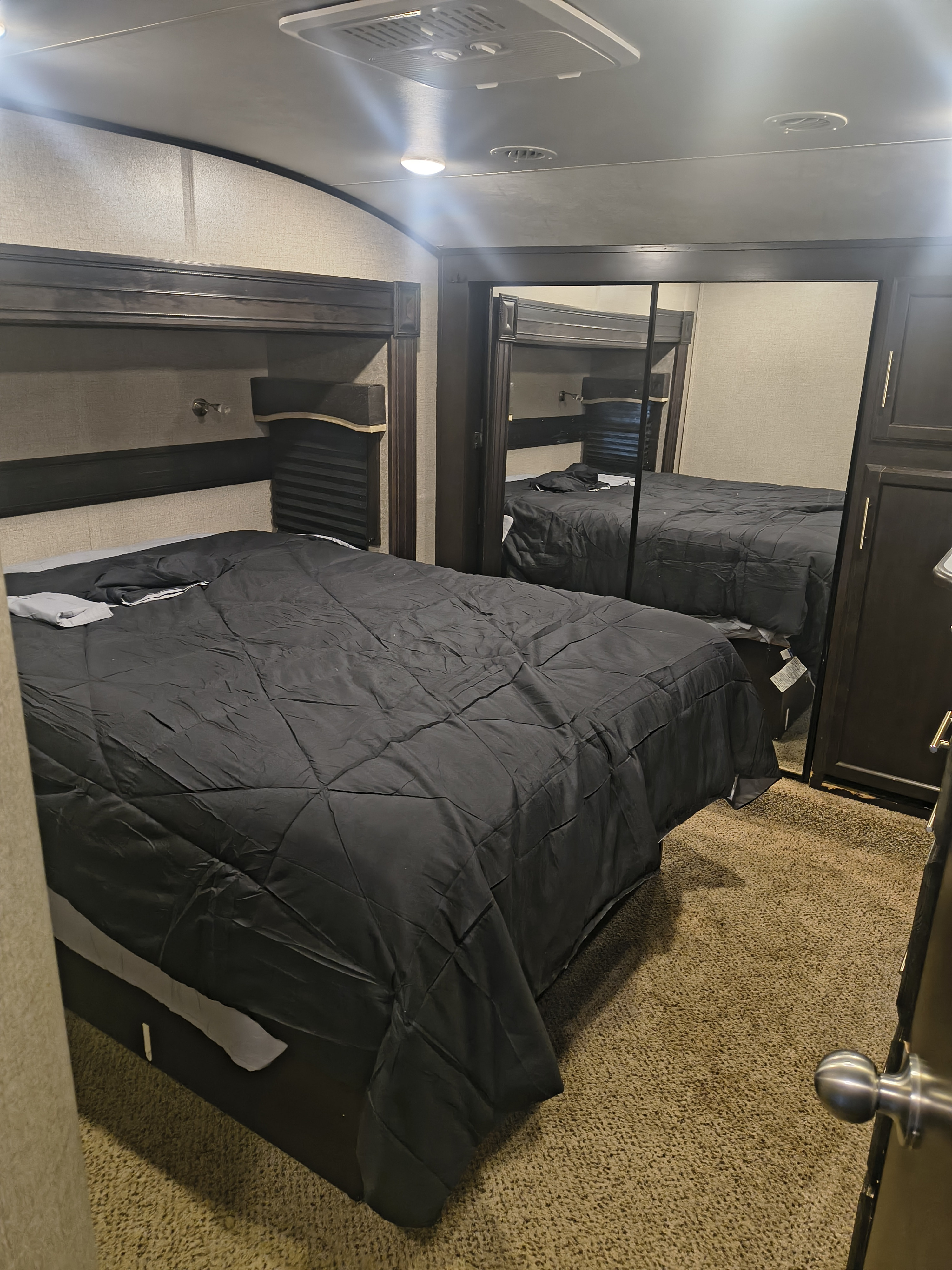Spacious RV rental bedroom with a bed covered in dark bedding, a mirrored wardrobe, and light brown carpet.. Jayco Eagle 2019
