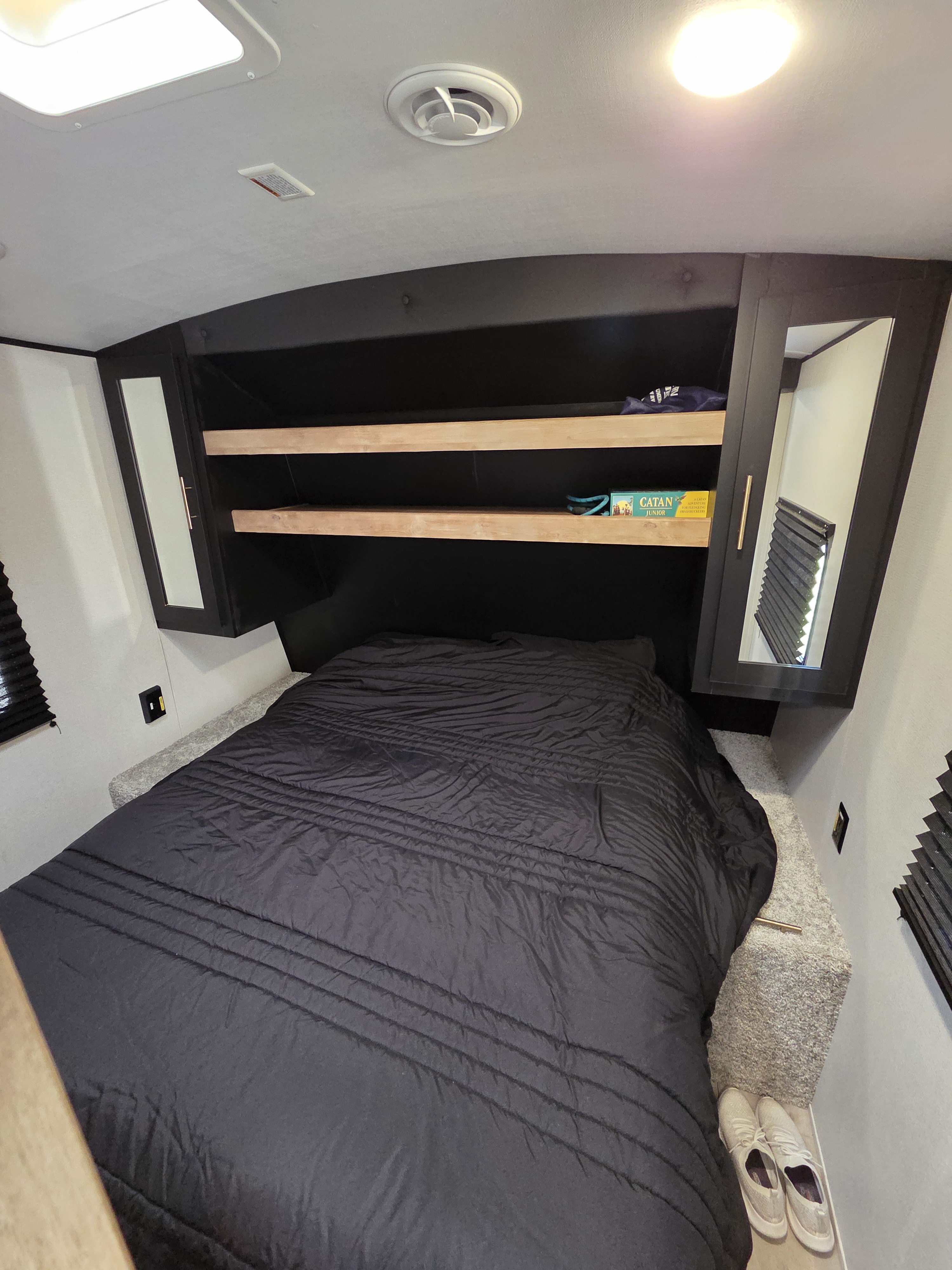 Cozy rv rental bedroom featuring a large bed with black comforter, overhead storage shelves, and mirrored cabinets.. Keystone RV Springdale 2022